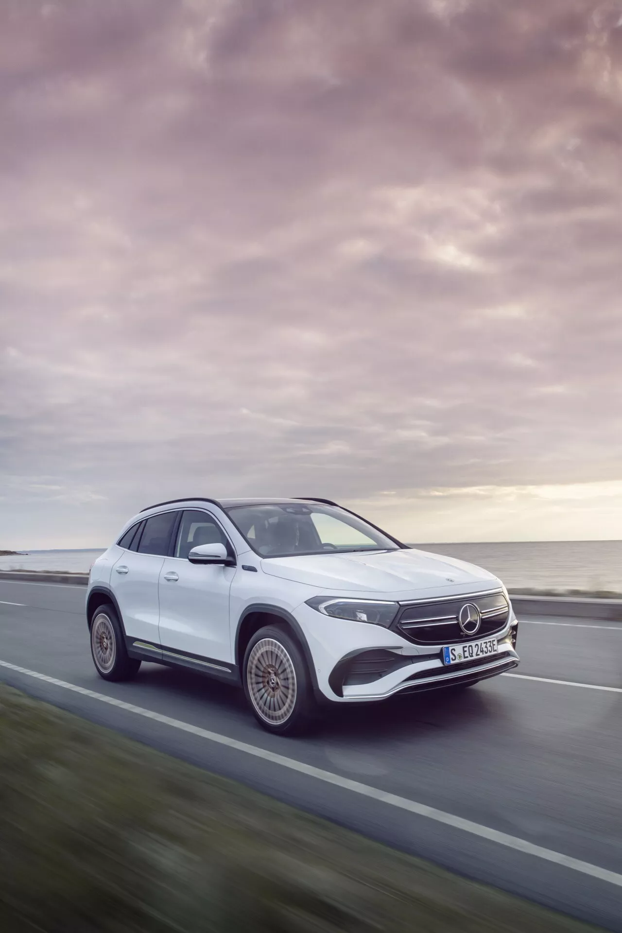2021 Mercedes-Benz EQA in motion, featuring a dynamic three-quarter front angle view showcasing the vehicle's design, LED headlights, stylized alloy wheels, and aerodynamic silhouette against a serene sunset backdrop