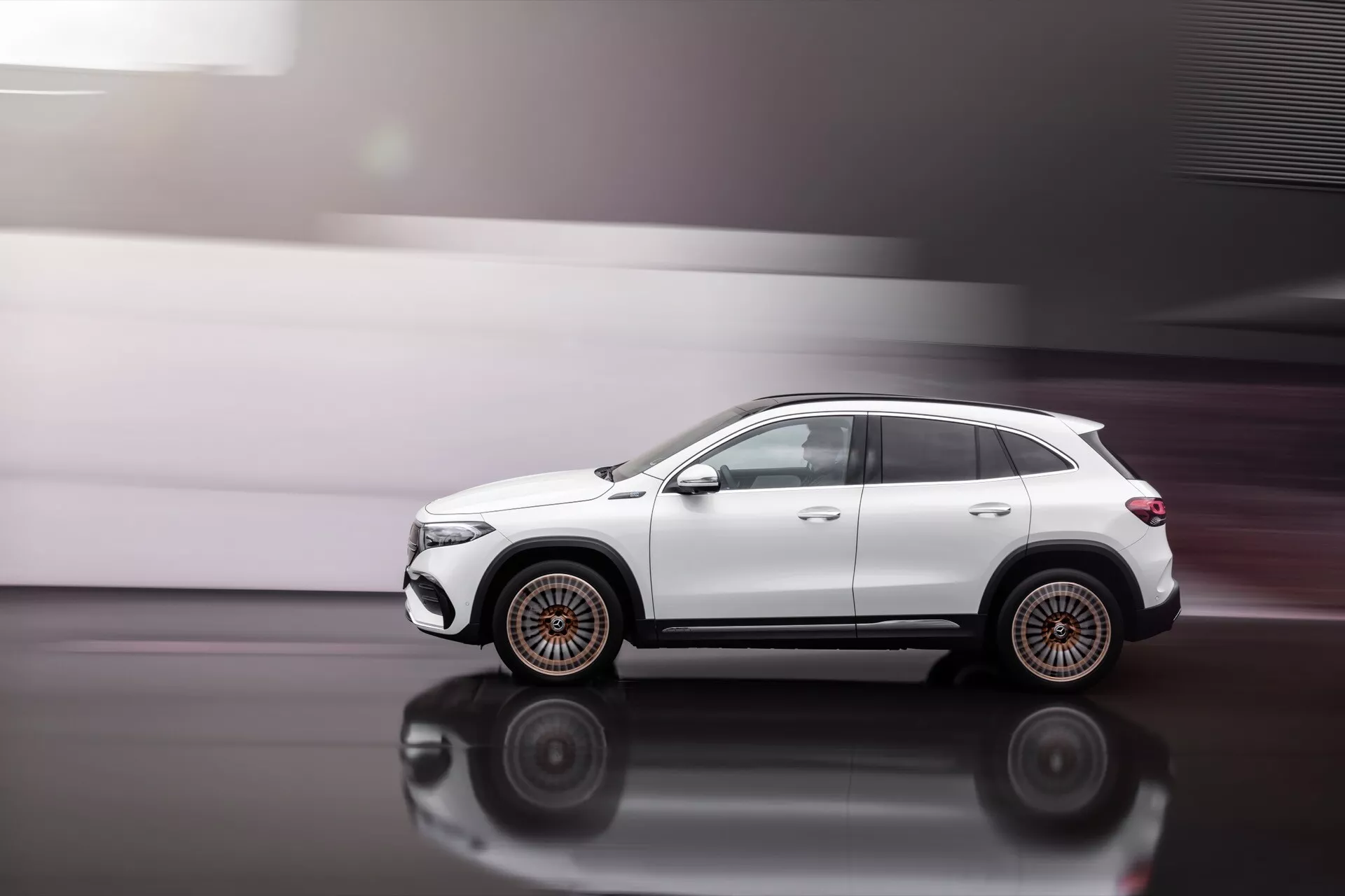 2021 Mercedes-Benz EQA dynamic side profile in motion on polished floor highlighting multi-spoke wheels, folded mirrors, roof rails, and sculpted body lines with privacy tinted windows, showcasing off-road stance and potential technology features like automatic folding mirrors and satellite antenna.