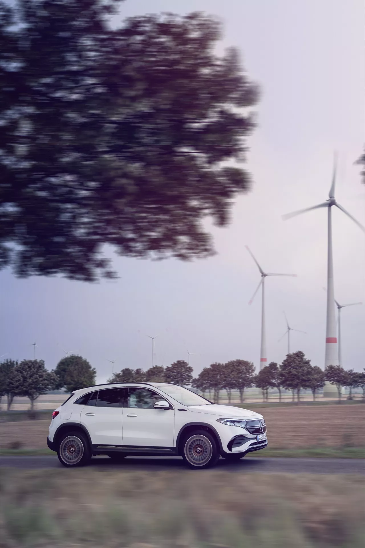 2021 Mercedes-Benz EQA in motion, side profile view showcasing luxury design and aerodynamics, with wind turbines in the background indicating eco-friendly technology