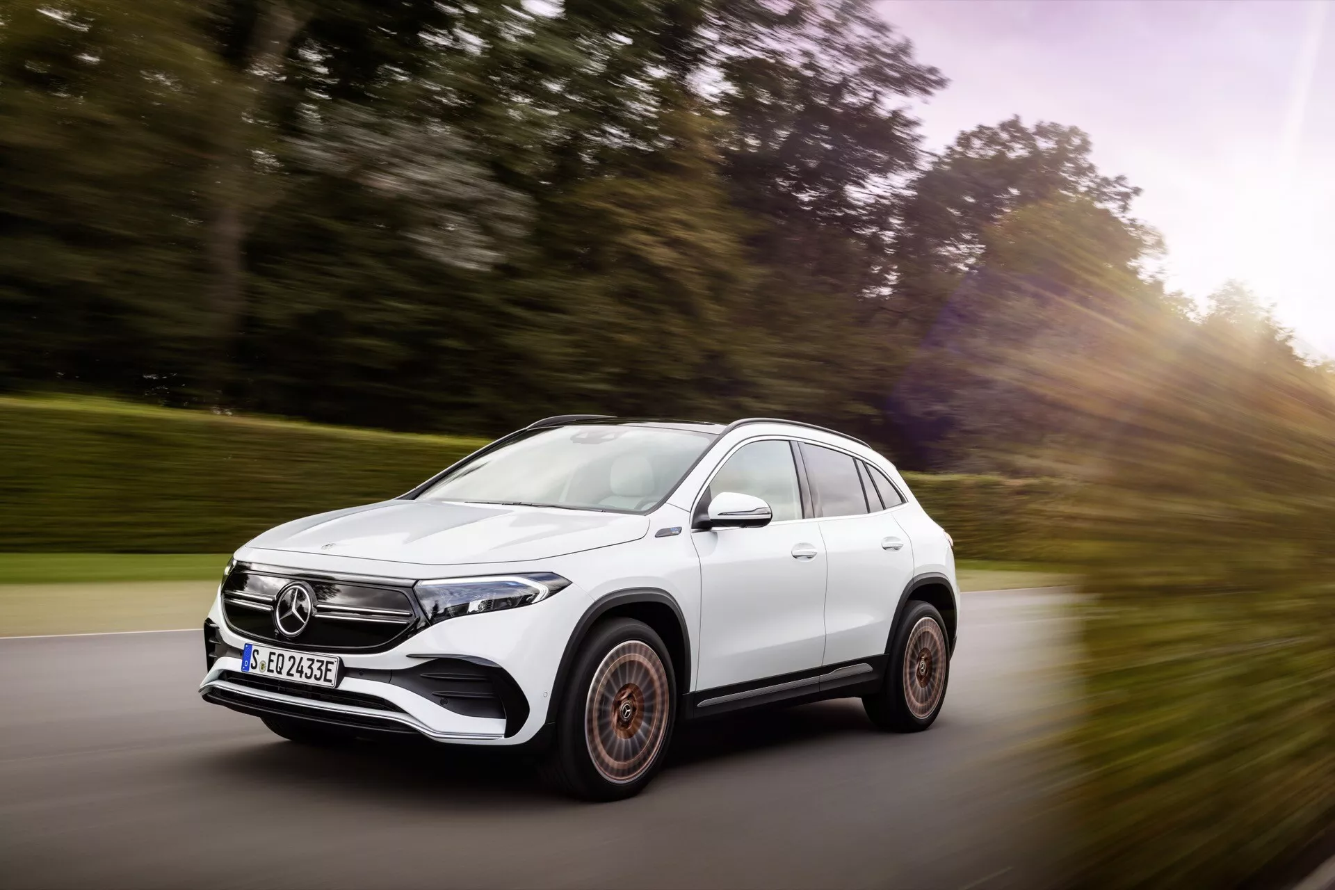 2021 Mercedes-Benz EQA white SUV in motion, front three-quarter view highlighting dynamic stance, aerodynamic design, LED headlights, and distinctive alloy wheels on a scenic road