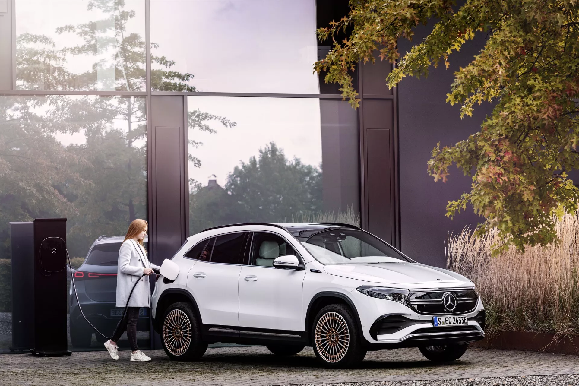 2021 Mercedes-Benz EQA parked at an electric charging station, showcasing its sleek white design, aerodynamic wheel pattern, and hybrid capabilities in a sustainable environment