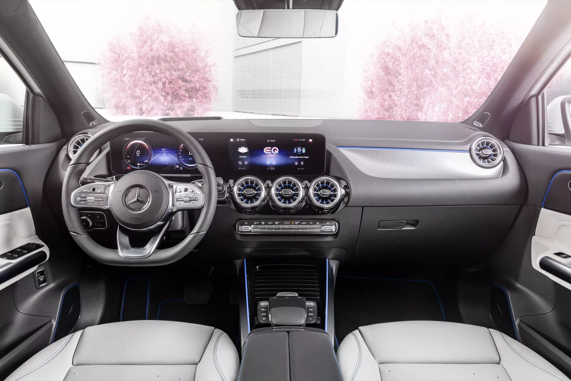 2021 Mercedes-Benz EQA interior view featuring the dashboard, multifunction steering wheel with silver accents, digital instrument cluster, widescreen infotainment system, metallic finish air vents, dual-zone climate control, modern gear shift lever, and luxurious two-tone leather seats with accent stitching from the rear seat perspective