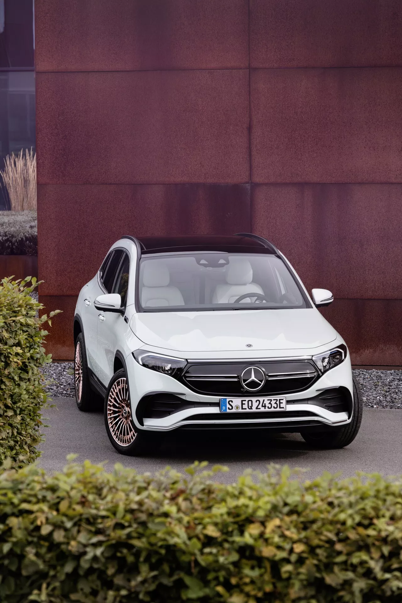 2021 Mercedes-Benz EQA in white, photographed from a frontal three-quarter perspective showcasing the vehicle's aerodynamic design, LED headlights, distinctive front grille with a large emblem, sporty front bumper, and unique wheel design on a contrasting textured background