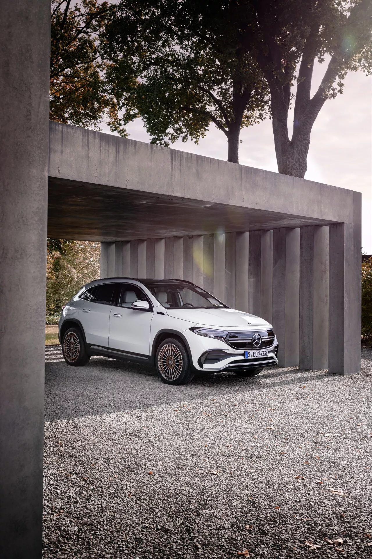 2021 Mercedes-Benz EQA parked under a minimalist concrete structure, showcasing its sleek LED headlights, distinctive front grille with emblem, aerodynamic white body, and intricate alloy wheels from a low angle three-quarter front view.
