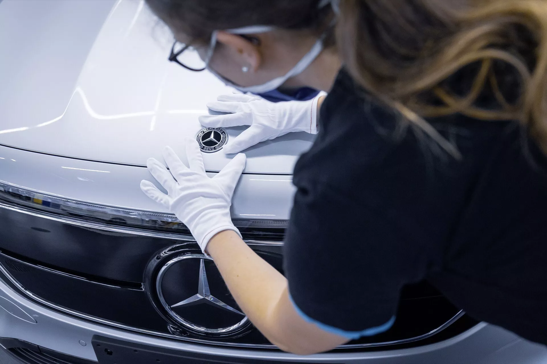 Close-up view of a Mercedes-Benz EQA 2021 front grille and emblem with a person in white gloves adjusting the emblem, highlighting the vehicle's premium craftsmanship and design