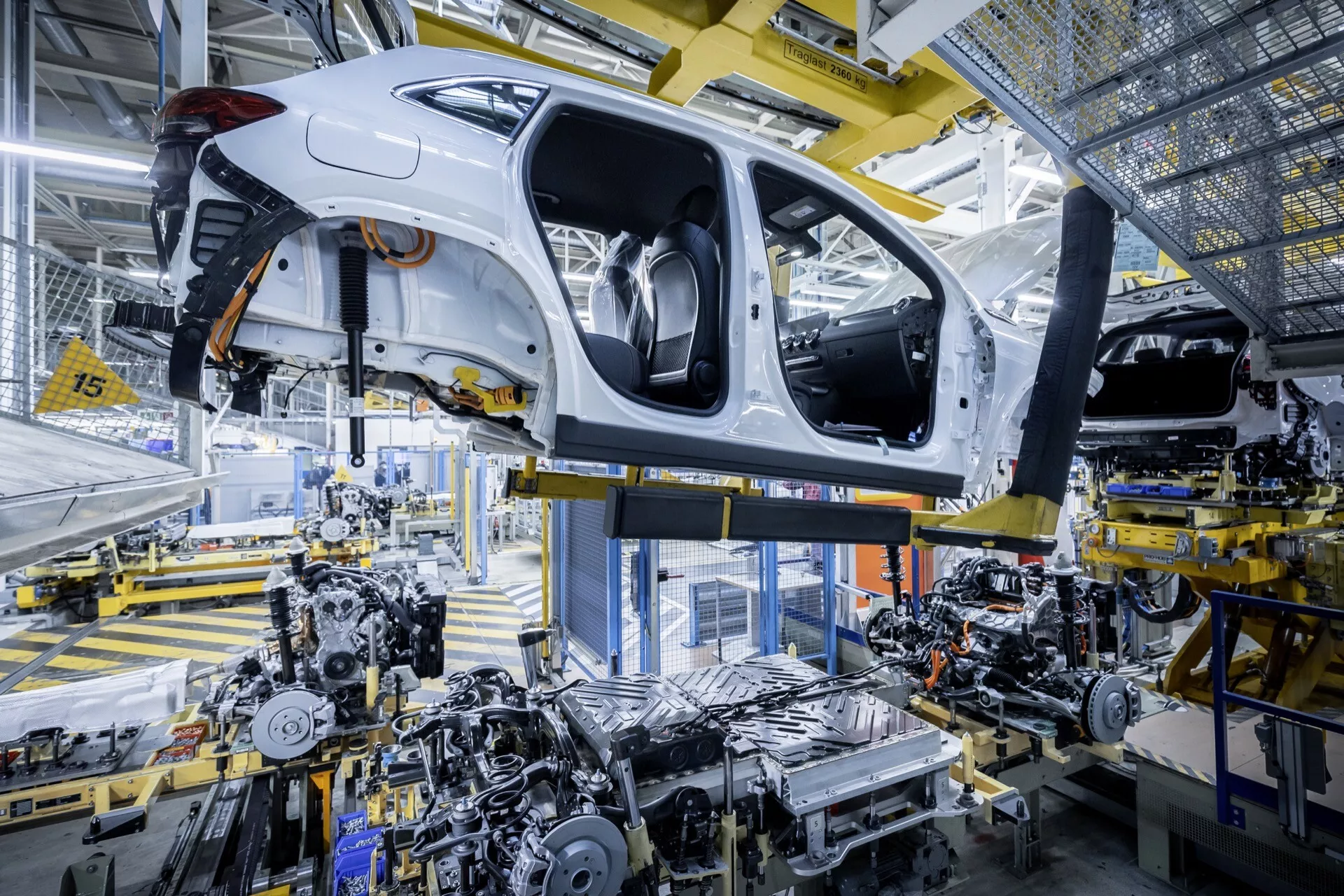 2021 Mercedes-Benz EQA (243) in white, undergoing assembly in an automotive plant, showcasing its chassis, undercarriage, and advanced robotic assembly technology