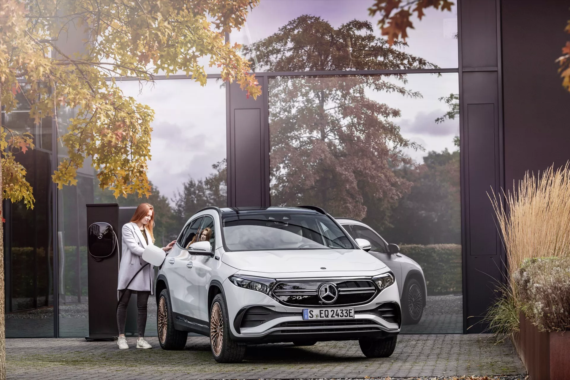 2021 Mercedes-Benz EQA SUV in residential driveway, featuring LED headlamps, alloy wheels, electric badge, and person demonstrating keyless entry, surrounded by autumn trees