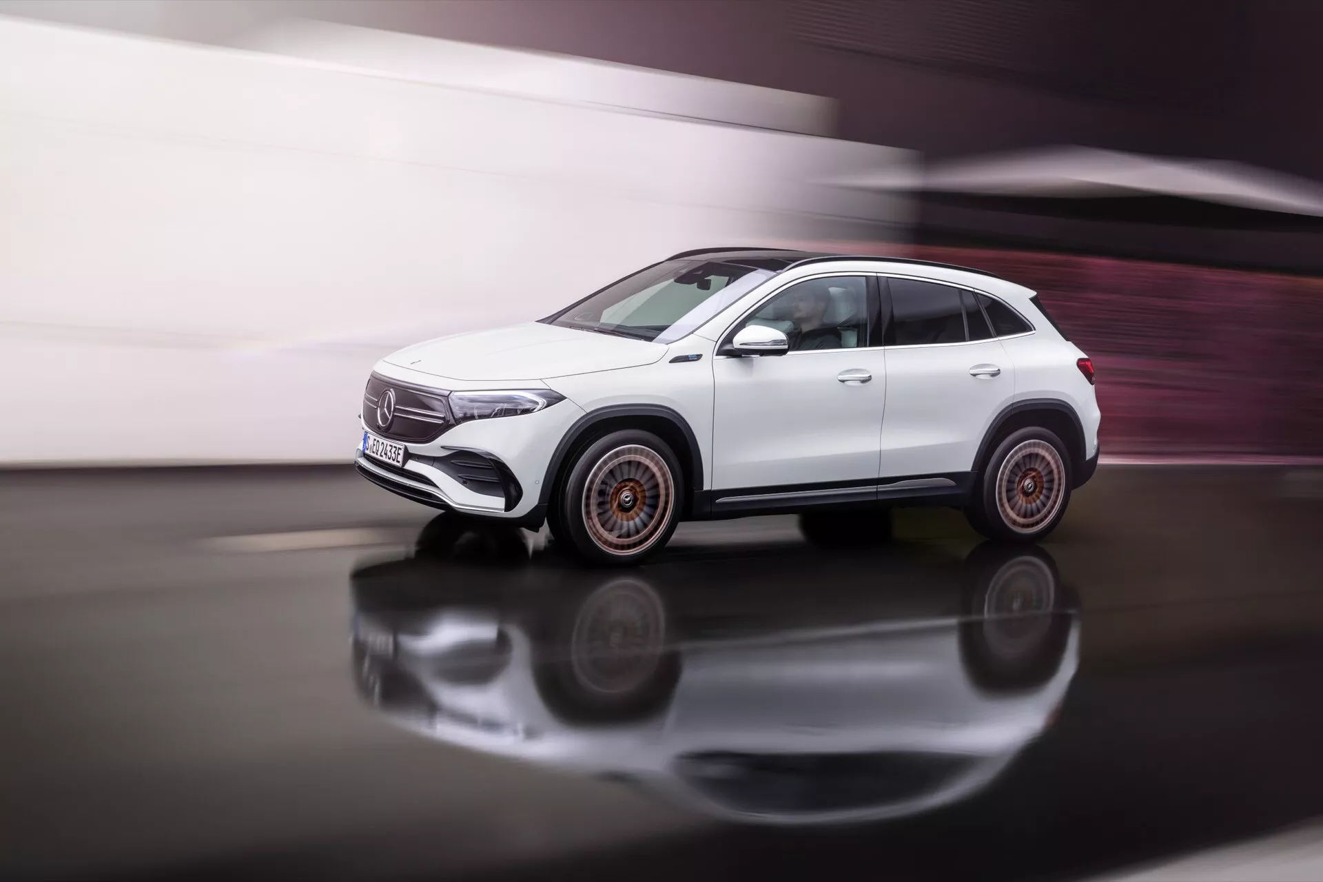 2021 Mercedes-Benz EQA white SUV in motion on reflective surface with dynamic side view showcasing design lines, window shapes, doors, and unique wheel design with subtle motion blur and copper accents