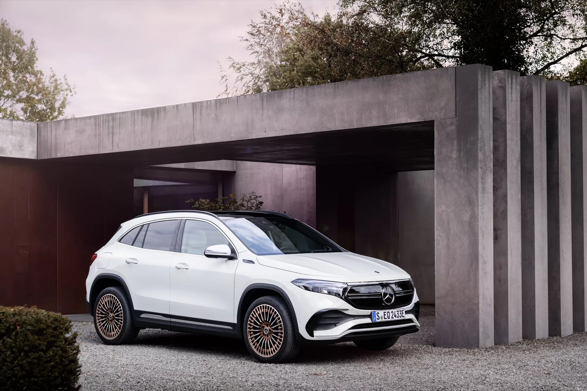 2021 Mercedes-Benz EQA white SUV parked in a modern driveway with a stylized residential carport backdrop, showcasing a front three-quarter view emphasizing its front grille, LED headlights, side bodywork, wheels, and windows