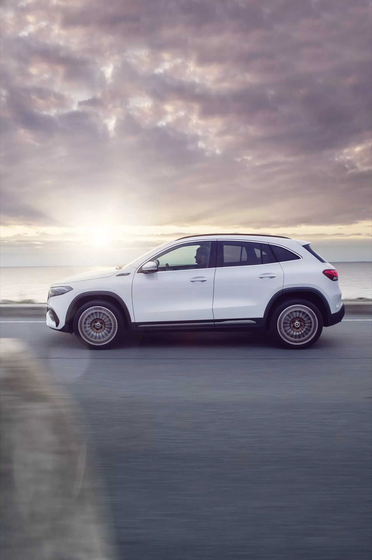 2021 Mercedes-Benz EQA white SUV in profile view showing motion blur, captured at sunrise or sunset with a focus on design features and modern technology.