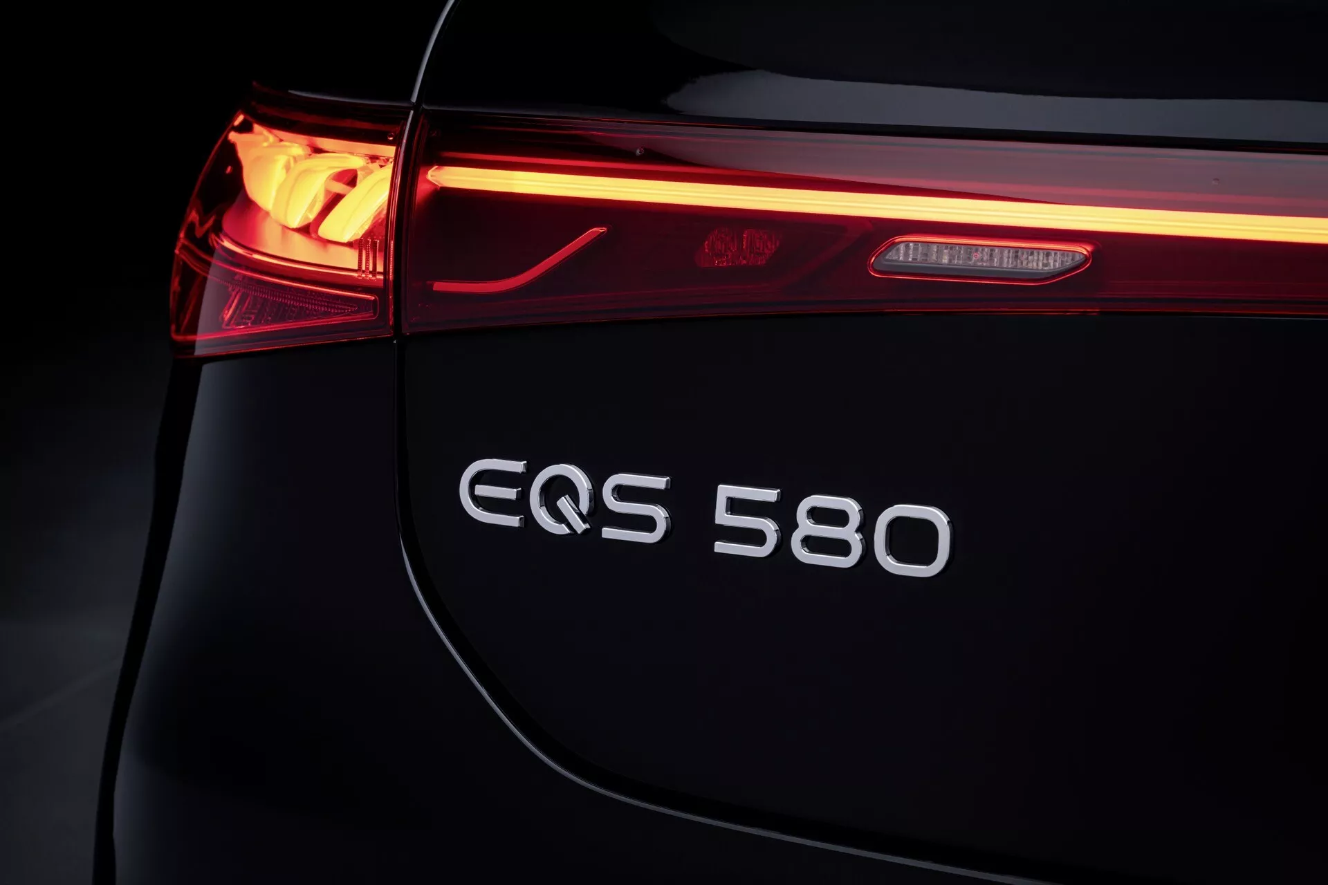 Close-up of the rear left view of a Mercedes-Benz EQS 2024, highlighting the LED tail light, EQS 580 badge, and sleek trunk design, symbolizing luxury and electric innovation.