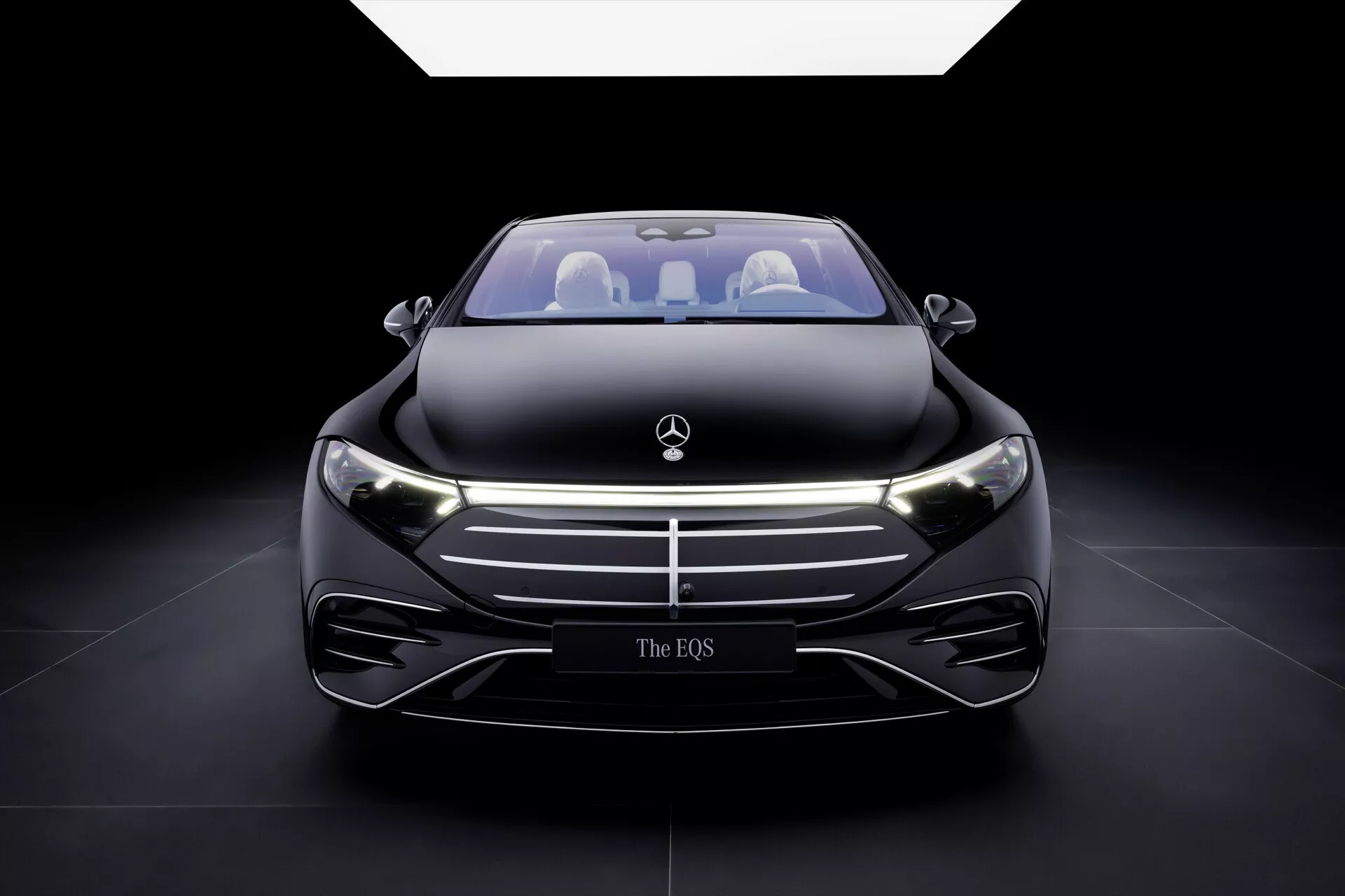 Front view of 2024 Mercedes-Benz EQS facelift with illuminated LED headlights and emblem, showcasing sleek aerodynamic design and advanced technology features against a black background