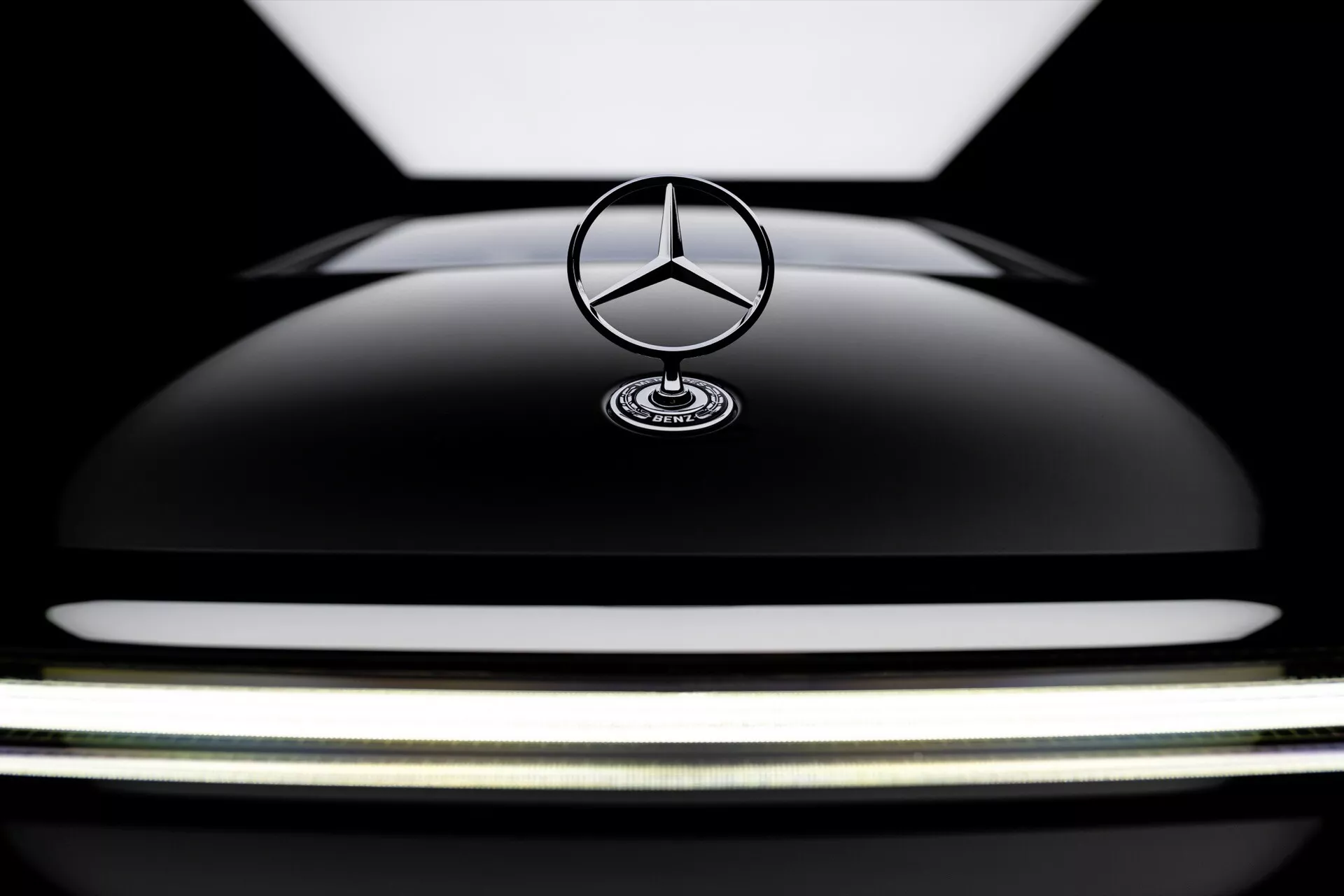 Close-up view of the 2024 Mercedes-Benz EQS facelift with focus on the glossy black hood and the iconic stand-up star emblem, showcasing the vehicle's luxury design and sleek curvature.