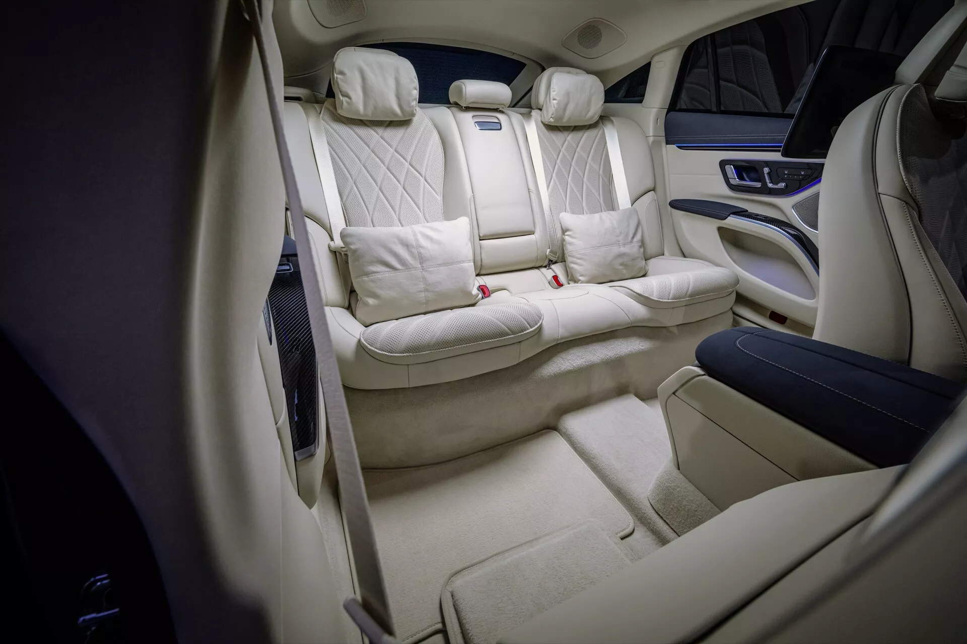 Interior view of the 2024 Mercedes-Benz EQS facelift showcasing the luxurious rear cabin with quilted diamond pattern seats, light cream upholstery, premium center console, extensive legroom, and ambient lighting