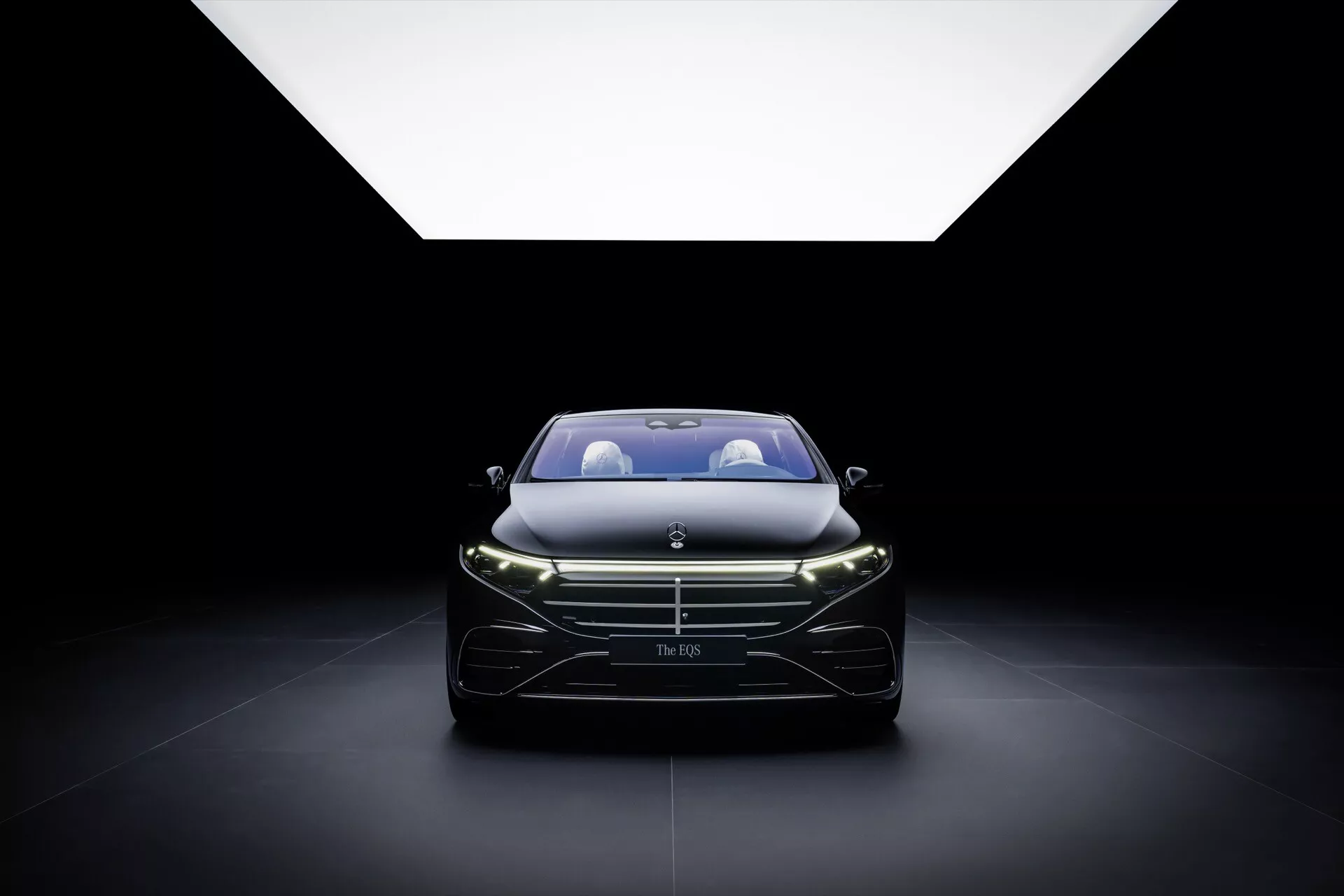 2024 Mercedes-Benz EQS facelift model displayed prominently with a focus on the grille, headlights, and sleek front design, highlighted by soft overhead lighting against a dark backdrop, capturing the essence of luxury and modern automotive craftsmanship.