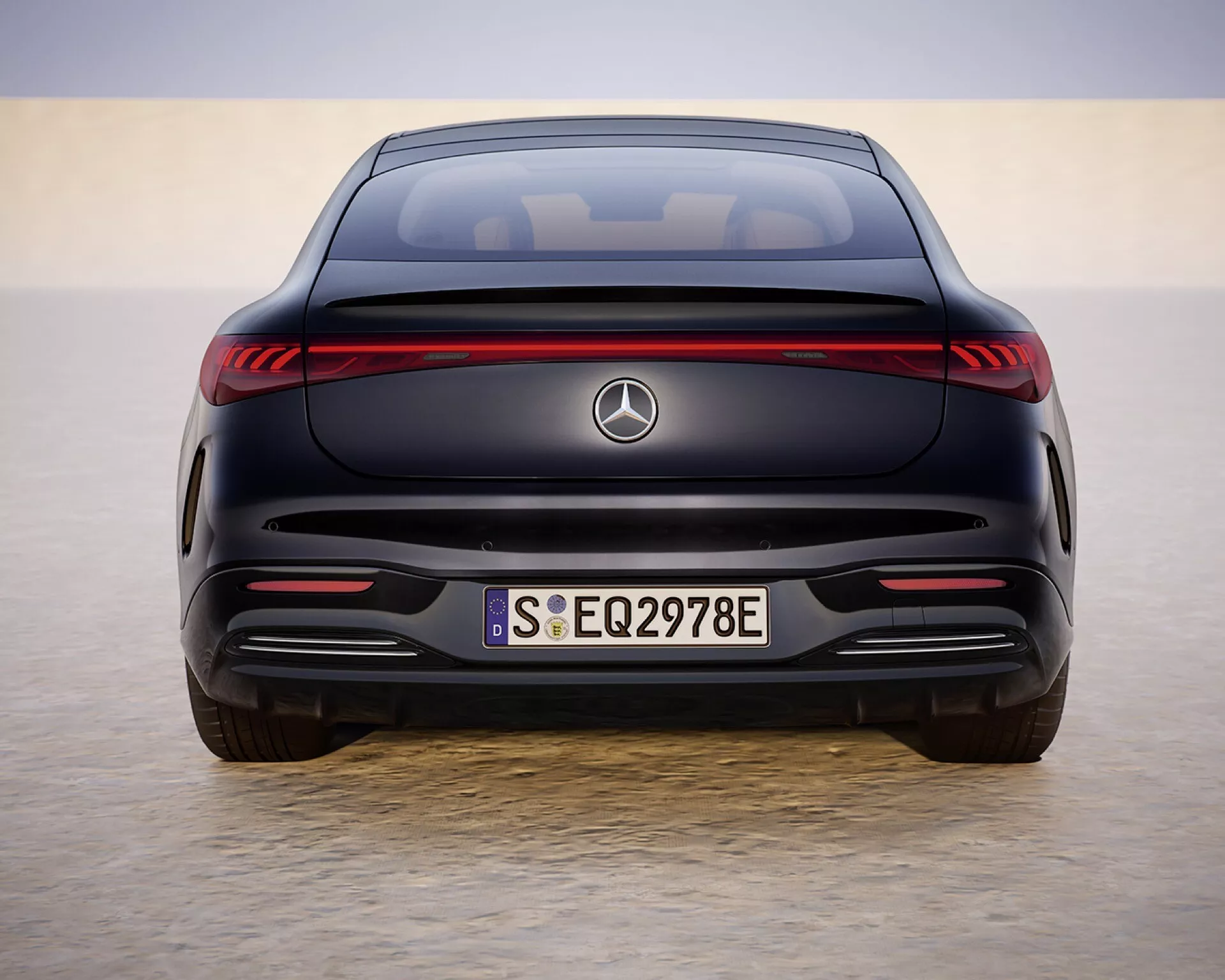 Rear view of the 2024 Mercedes-Benz EQS 297 facelift model in a desert-like setting, showcasing LED taillights, EQ badging, and sporty bumper design under daylight