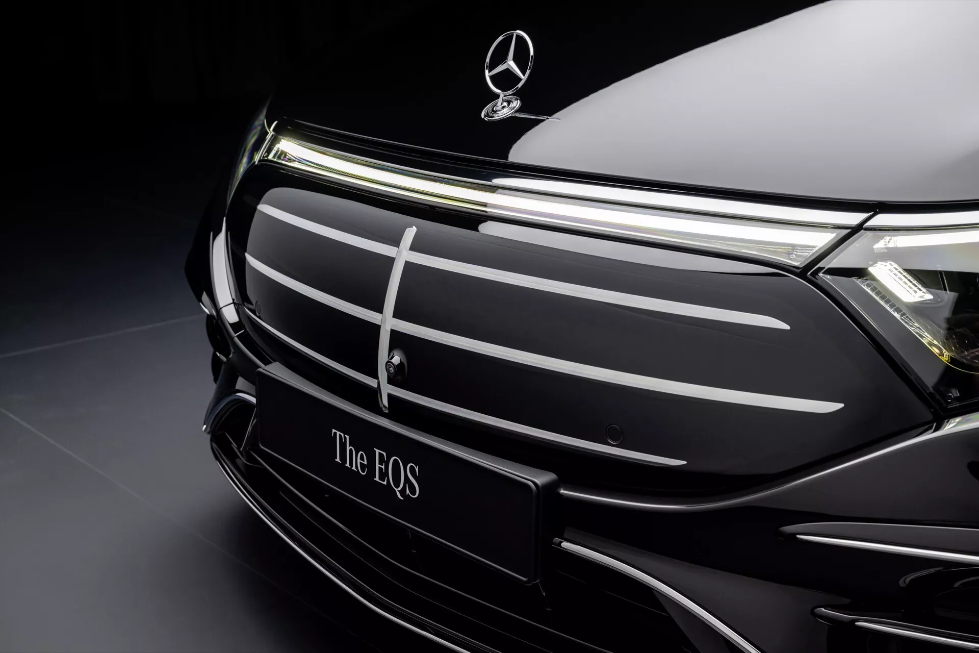 Close-up view of the Mercedes-Benz EQS 2024 facelift model showcasing the grille area and brand emblem against a sophisticated dark background, highlighting the vehicle's sleek design and electric luxury features