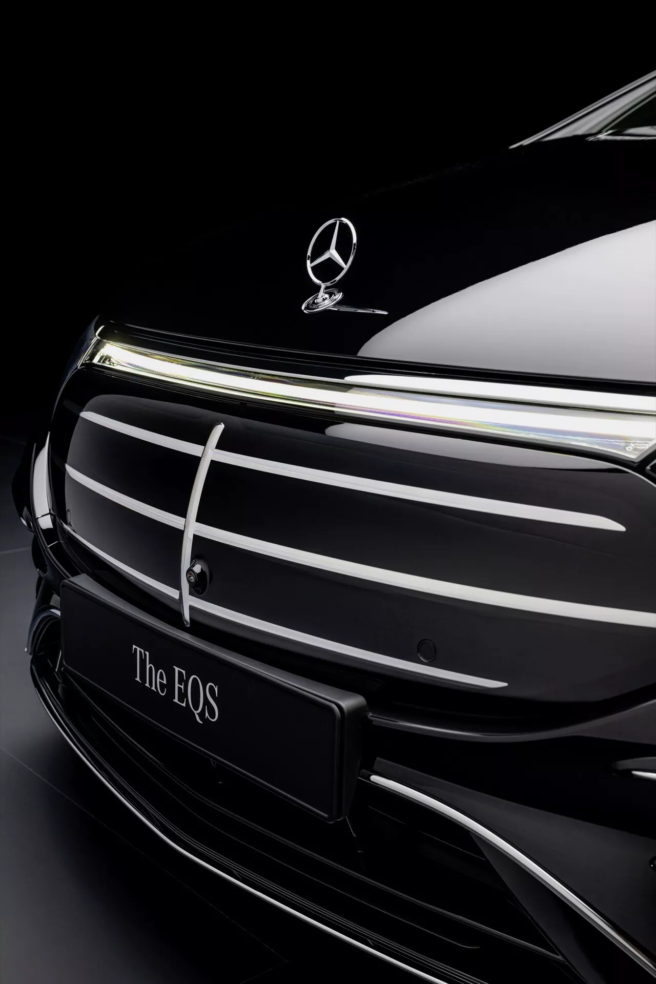 Close-up of the Mercedes-Benz EQS 2024 facelift front end with emblem and chrome grille against a dark background highlighting luxury and electric vehicle design