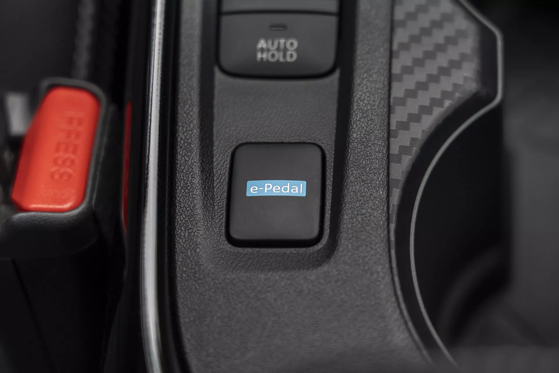 2019 Nissan Juke (F16) interior close-up highlighting the e-Pedal system switch for electric or hybrid drive control, with AUTO HOLD button and red seat belt clip visible suggesting advanced automotive technology and premium interior features