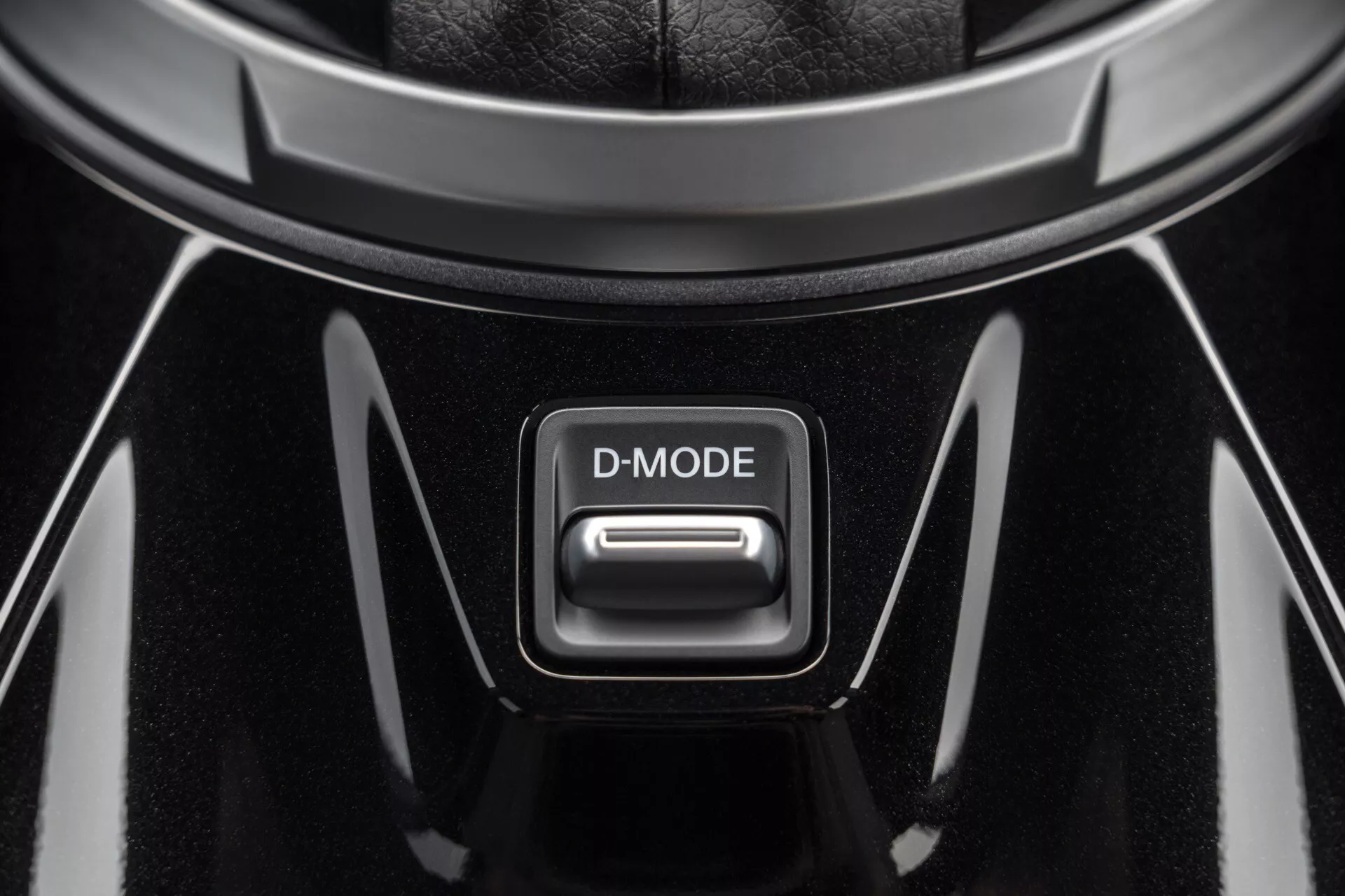 Close-up view of the D-MODE button in the central console of a 2019 Nissan Juke (F16), featuring a high-gloss black finish with chrome accents under top-down lighting
