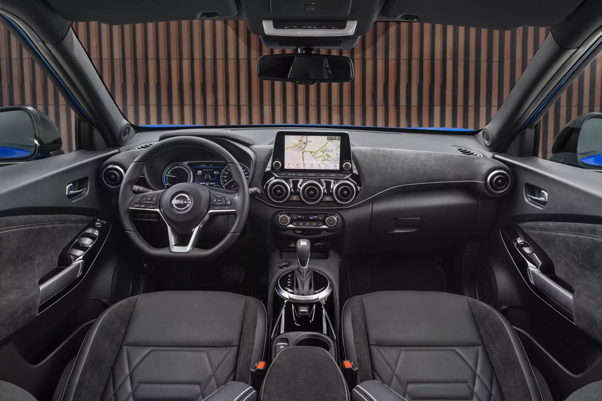 2019 Nissan Juke (F16) interior view from rear seat showcasing left-sided steering wheel with control buttons, centered touchscreen infotainment system with navigation, manual transmission gear shift, diamond-stitched seats, and sunroof controls