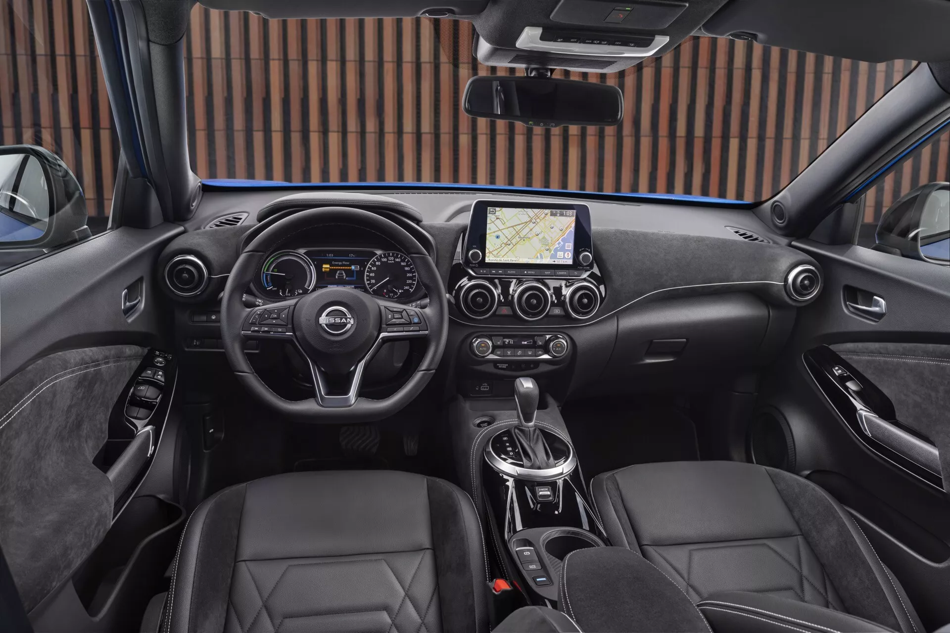 2019 Nissan Juke F16 interior view from the driver's perspective, featuring a modern three-spoke steering wheel with control buttons, combined digital and analog instrument cluster, central touchscreen infotainment system with navigation, dual-zone climate control, automatic transmission, leather bucket seats, and electronic parking brake.