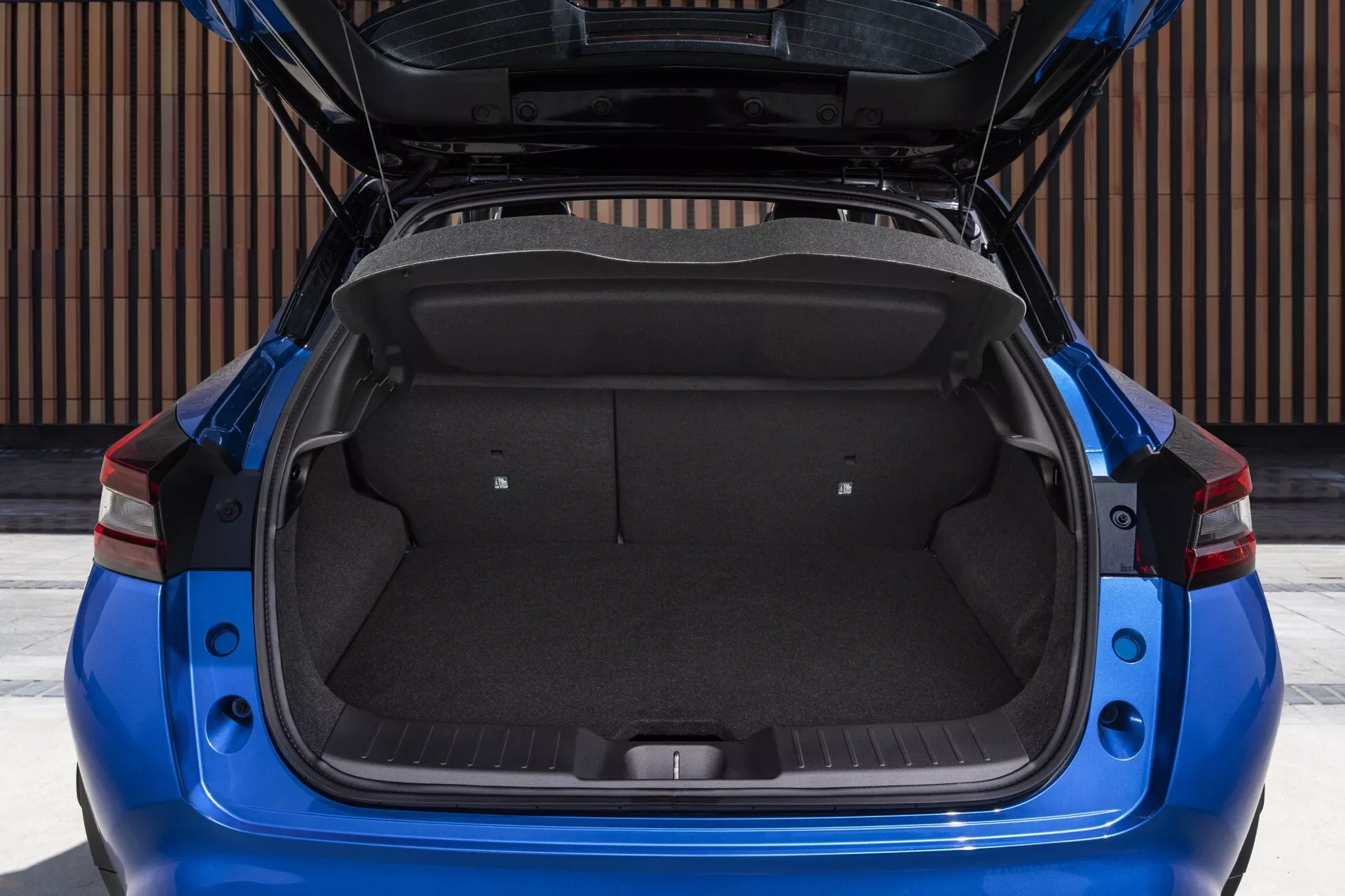 Direct rear view of a 2019 Nissan Juke (F16) highlighting the open trunk's spacious cargo area, showcasing a clean and well-maintained interior with standard carpet and maximized storage space due to folded rear seats. The vehicle's modern design is accentuated by sharp, angular LED taillights and a body-colored rear bumper, indicating a focus on practicality and style.