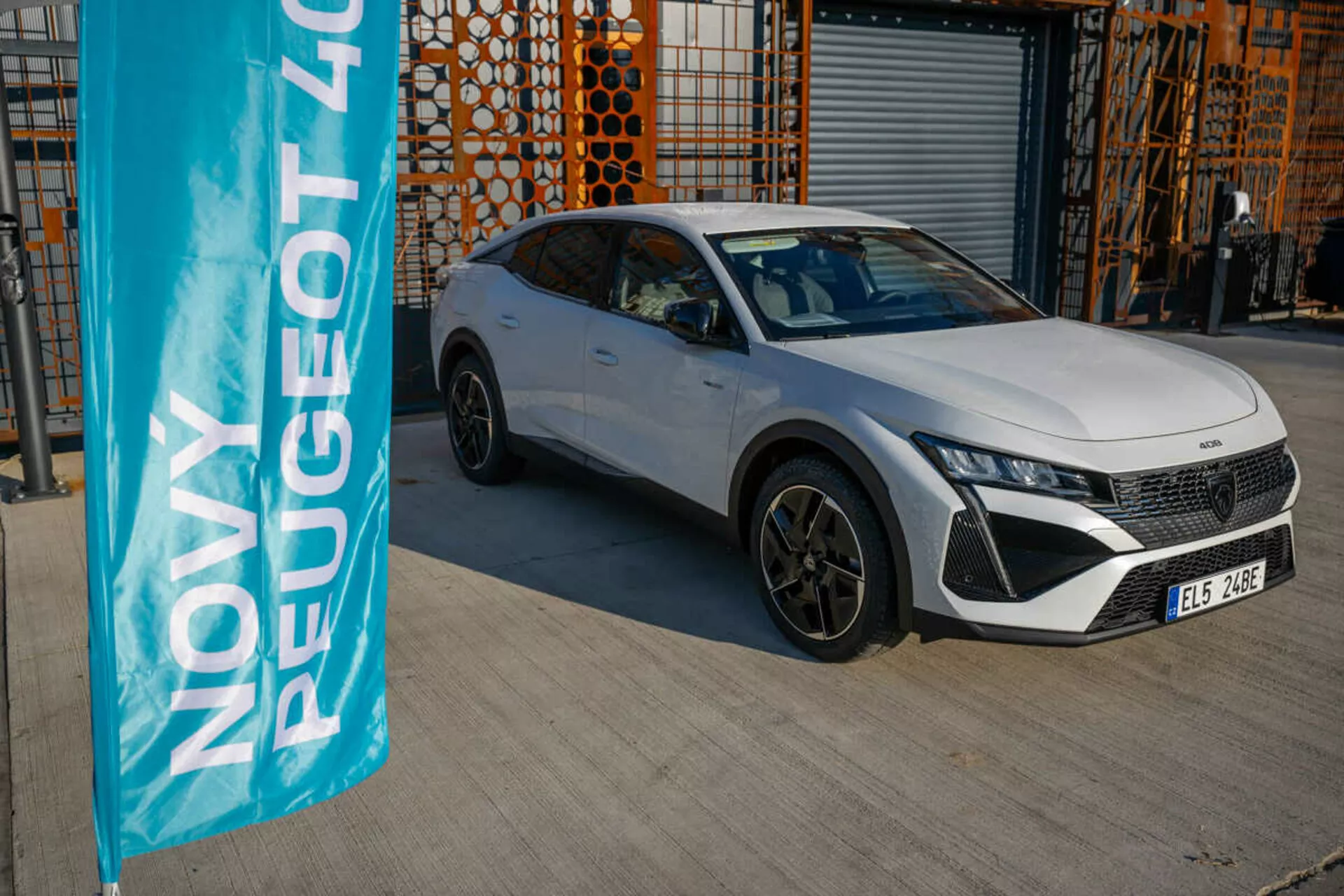2023 white Peugeot 408 parked outdoors with industrial architecture in background, showcasing the vehicle's design and technology features under natural daylight