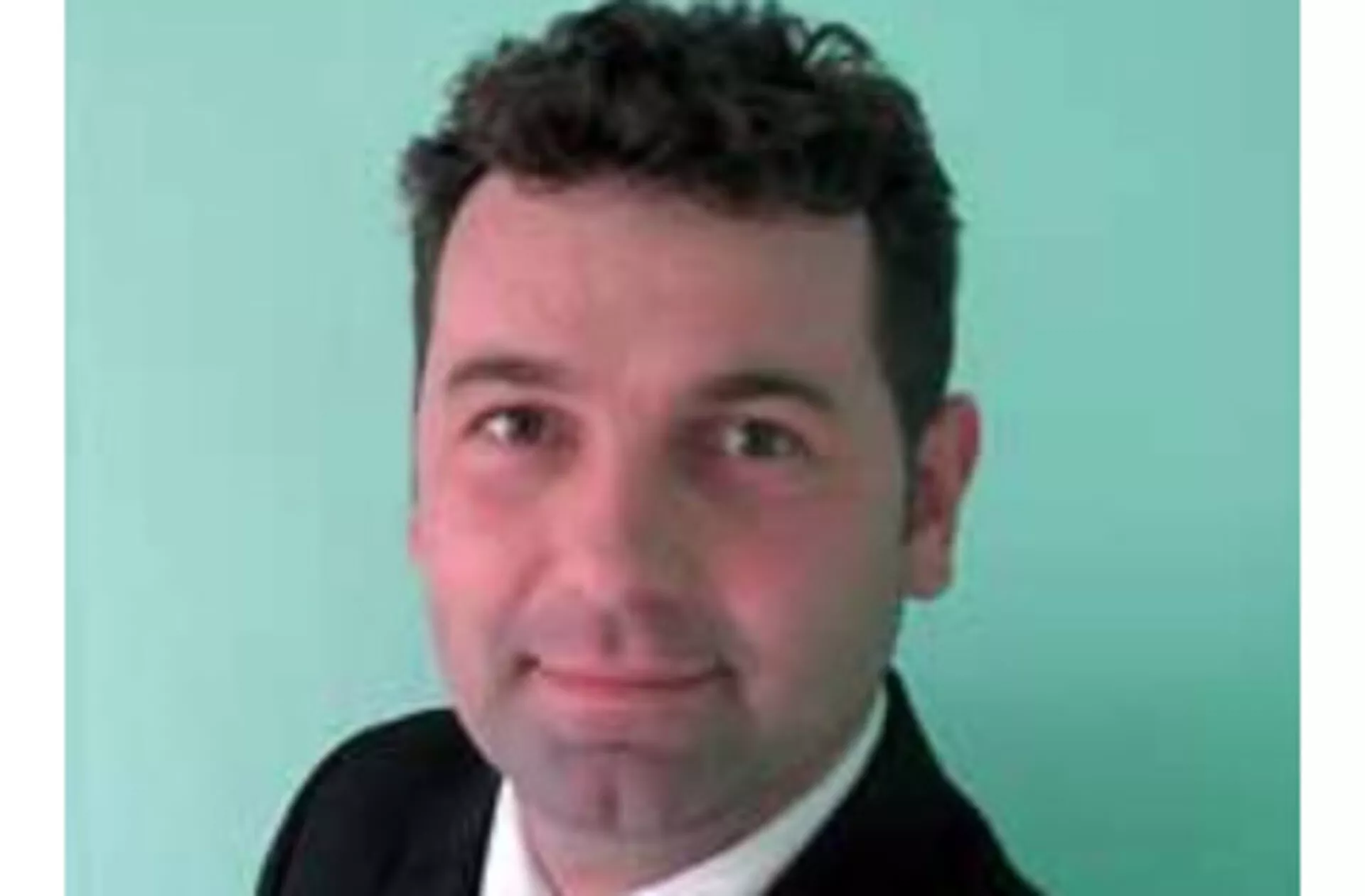 Professional photo of a male with short dark hair dressed in a suit against a light-colored background
