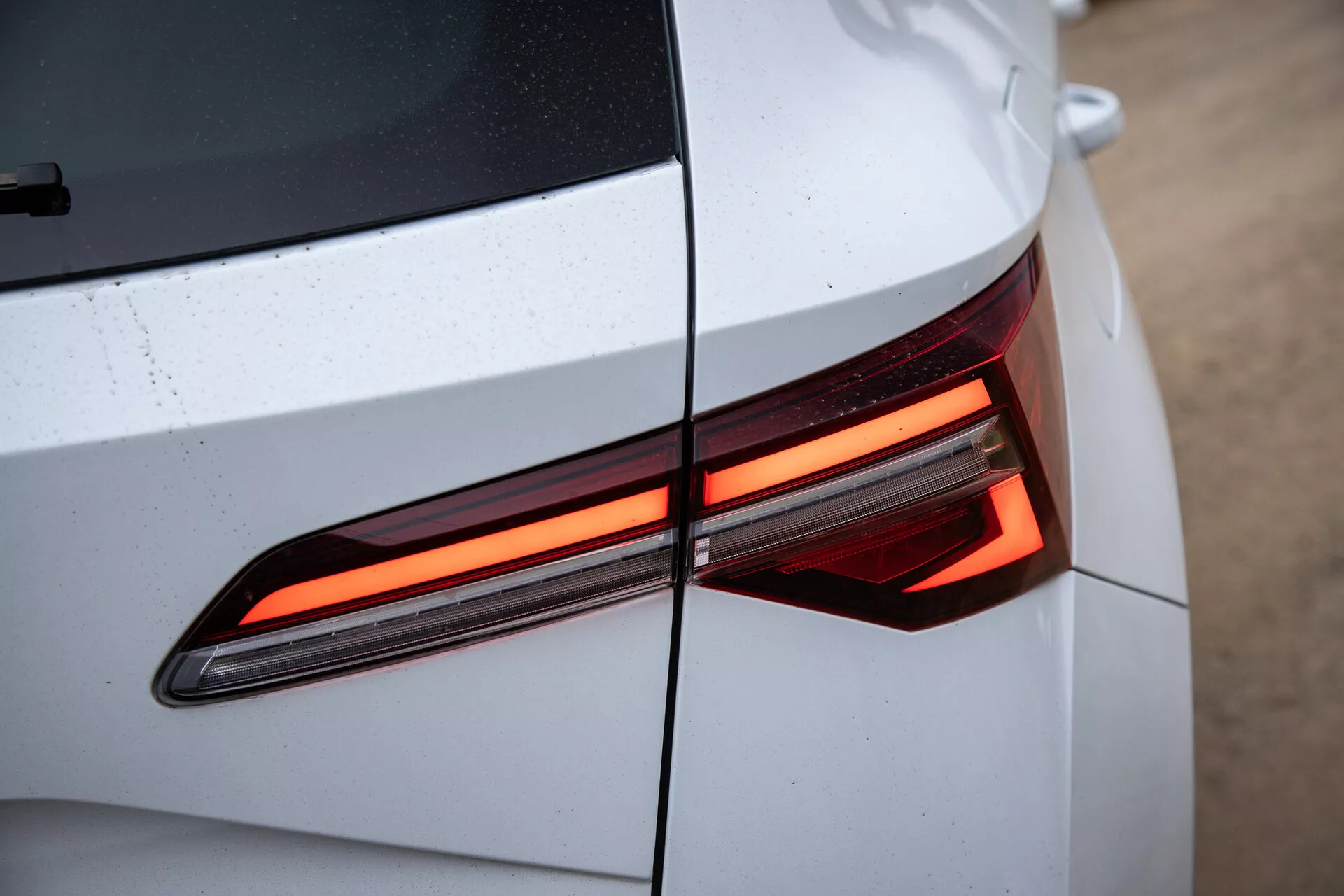 Close-up of the Skoda Karoq 2021's rear section showing the modern, LED tail light design, with an emphasis on the angular lines and glossy, light-colored car body with visible water droplets