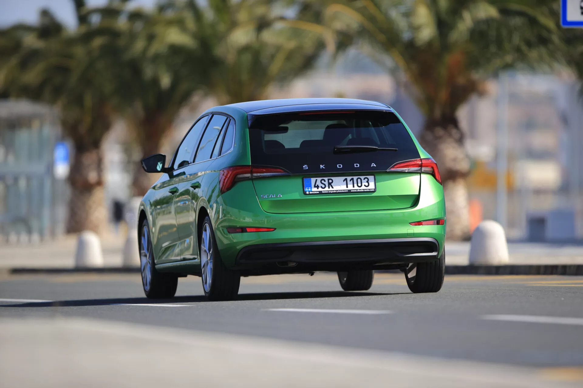 Rear view of a moving green Skoda Scala 2019 showcasing design lines, LED taillights, dual exhausts, and rear parking sensors, taken from a low angle with a shallow depth of field