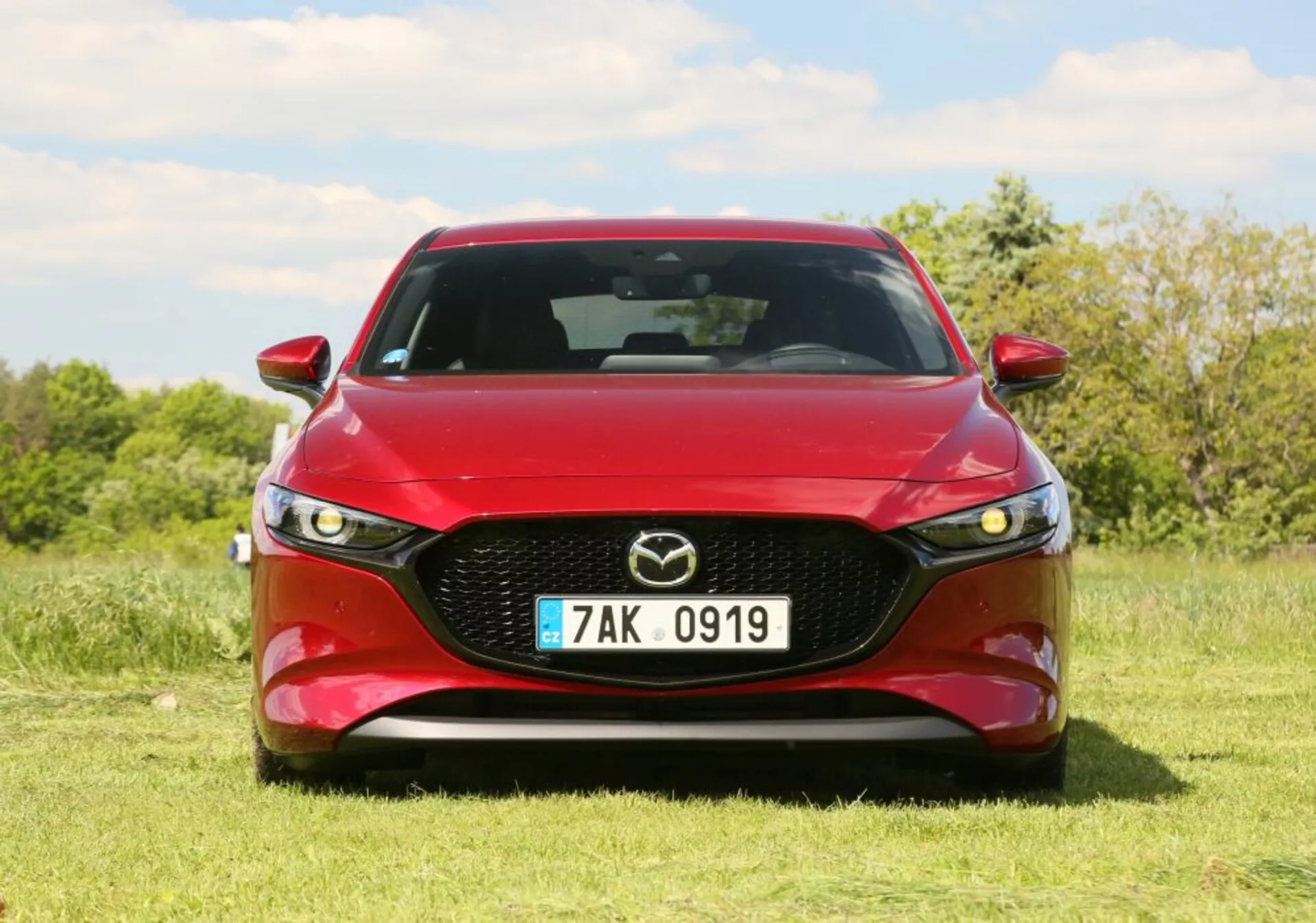 Red Mazda vehicle with LED headlights and chrome grille parked on grass under clear sky, showcasing sporty front-end design and vehicle aesthetics.