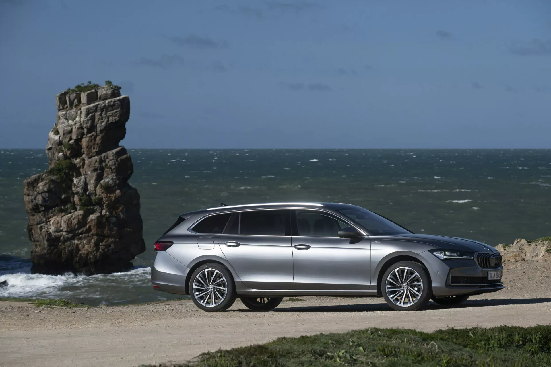 2024 Skoda Superb Combi parked by the ocean with side profile view showcasing design and technological features, with natural seaside landscape in the background