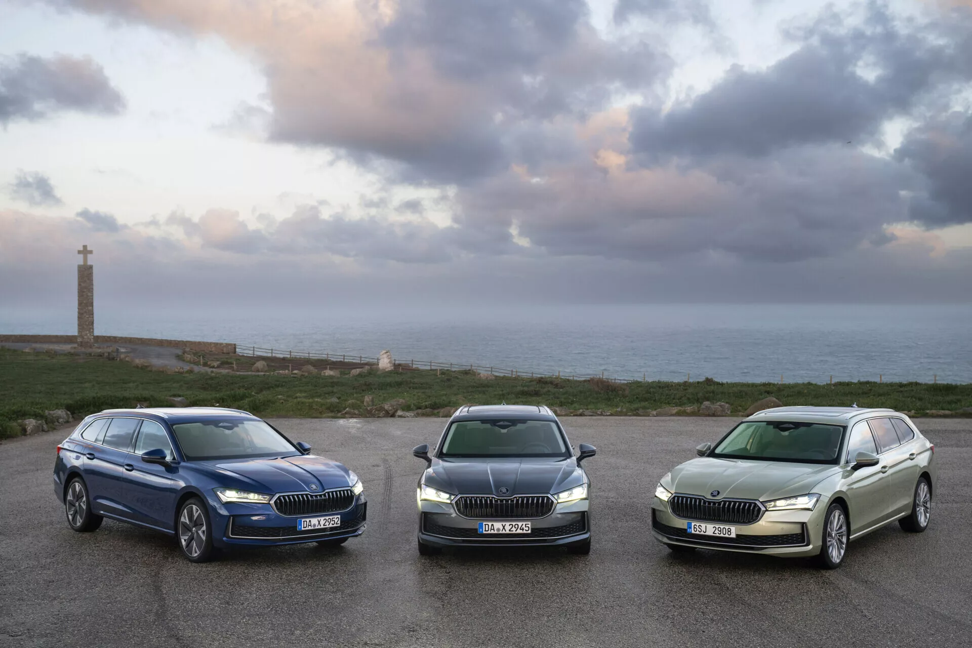 2024 Skoda Superb Combi models parked in a row facing the camera at sunrise, highlighting their grilles, headlights, and side profiles against a coastal landscape