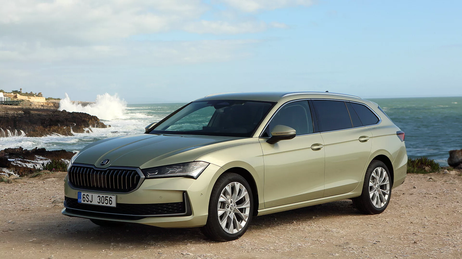 2024 Skoda Superb Combi showcased in a natural coastal setting, featuring a prominent grille, sleek LED headlights, advanced driver assists, and a stylish yet practical design with alloy wheels and roof rails