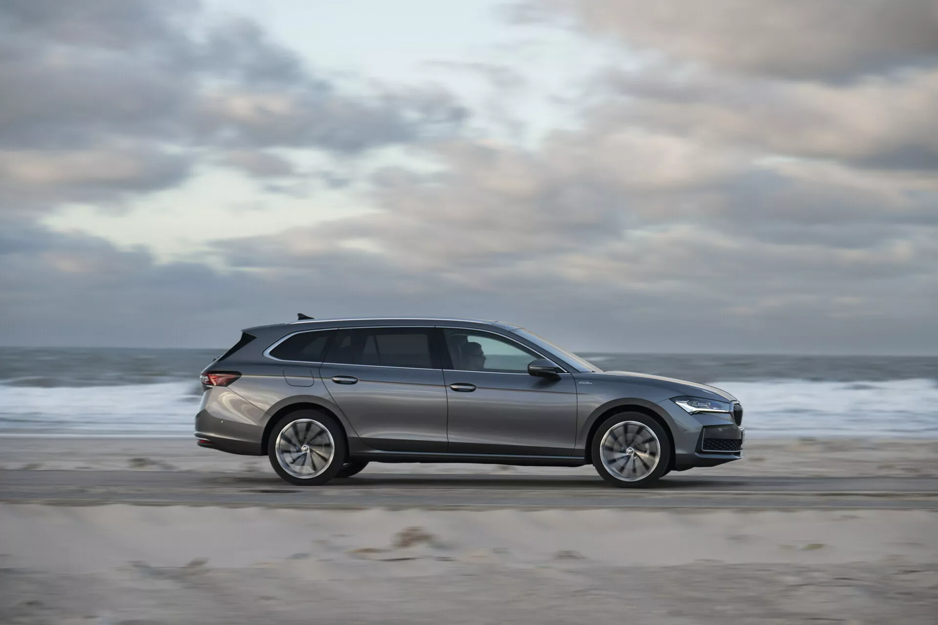 2024 Skoda Superb Combi parked on a beach with sandy and watery backdrop, highlighting its sleek design, modern LED lighting, and advanced technological features in a serene outdoor setting