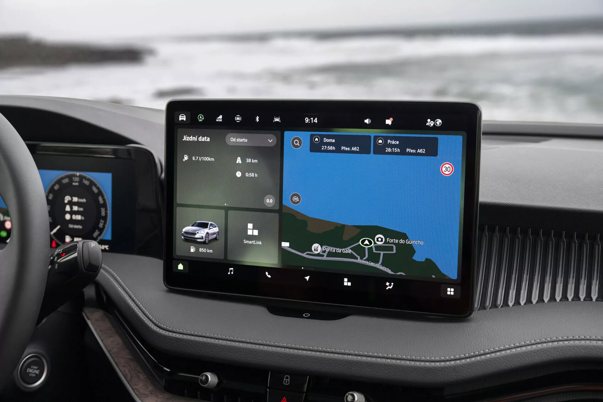 Interior view of the 2024 Skoda Superb Limousine highlighting the advanced infotainment system prominently mounted in the center of the dashboard. The touchscreen, roughly 10 to 12 inches in size, displays a navigation map and vehicle data. Visible are icons for various functionalities like climate control and vehicle settings, indicating a comprehensive infotainment system with potential Bluetooth, Wi-Fi, and smartphone integration. The overall luxurious design is apparent through high-quality materials and a hybrid instrument panel combining analog and digital elements.