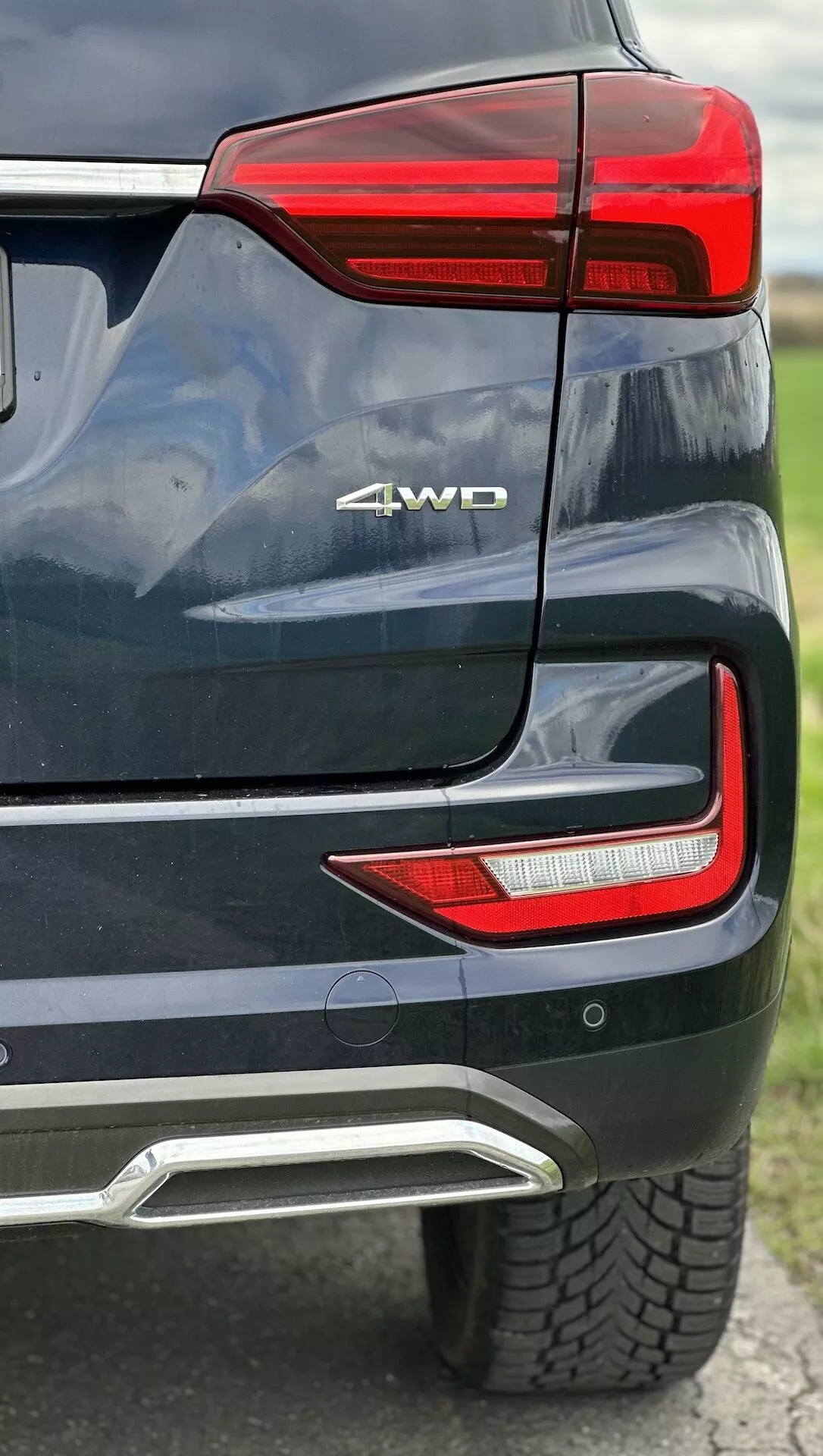 Detailed view of the 2021 SsangYong Rexton's rear corner showing LED rear light cluster, 4WD badge, parking sensor, integrated exhaust cover in metallic paint