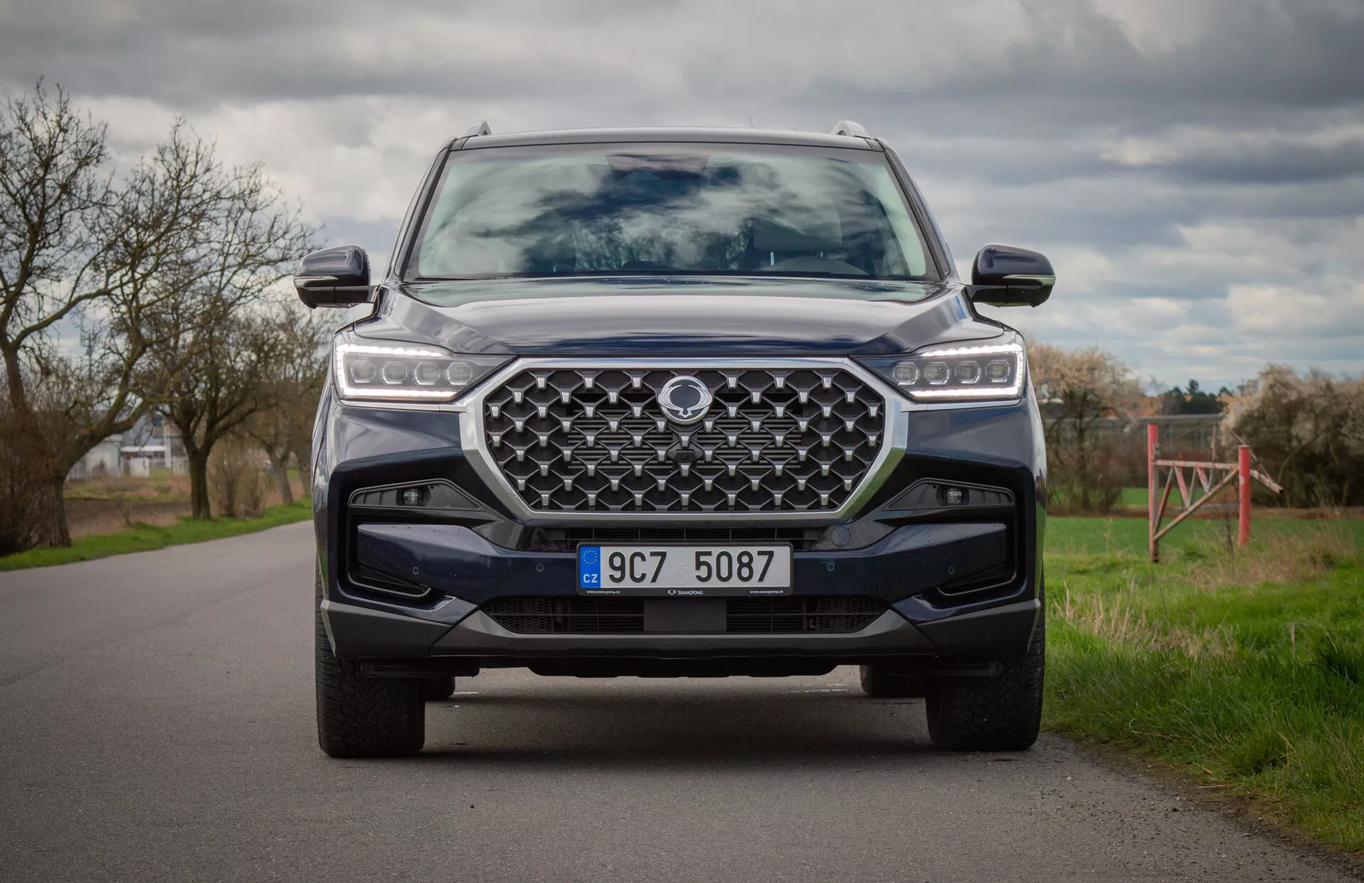2021 SsangYong Rexton modern SUV in color, captured from a kneeling position showcasing the vehicle's front end, LED headlights, large designed grille, front bumper with skid plate, and advanced driver assistance systems