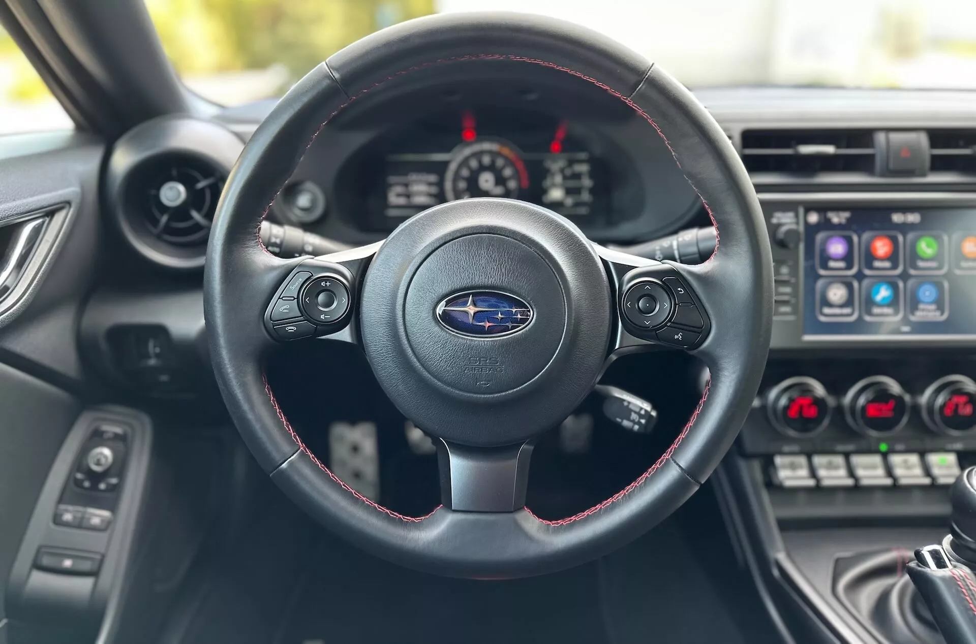 2023 Subaru BRZ interior view from driver's seat focusing on three-spoke steering wheel with red stitching, Subaru logo, and dashboard with instrument cluster and center console