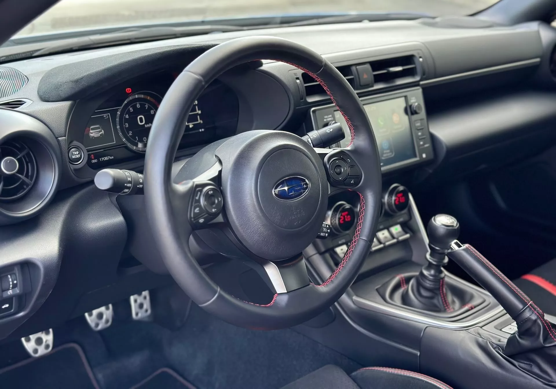 2023 Subaru BRZ interior focusing on the driver's side dashboard and cockpit with detailed view of the steering wheel, instrument cluster, center console with audio and climate controls, and manual gear shift with sporty red stitching