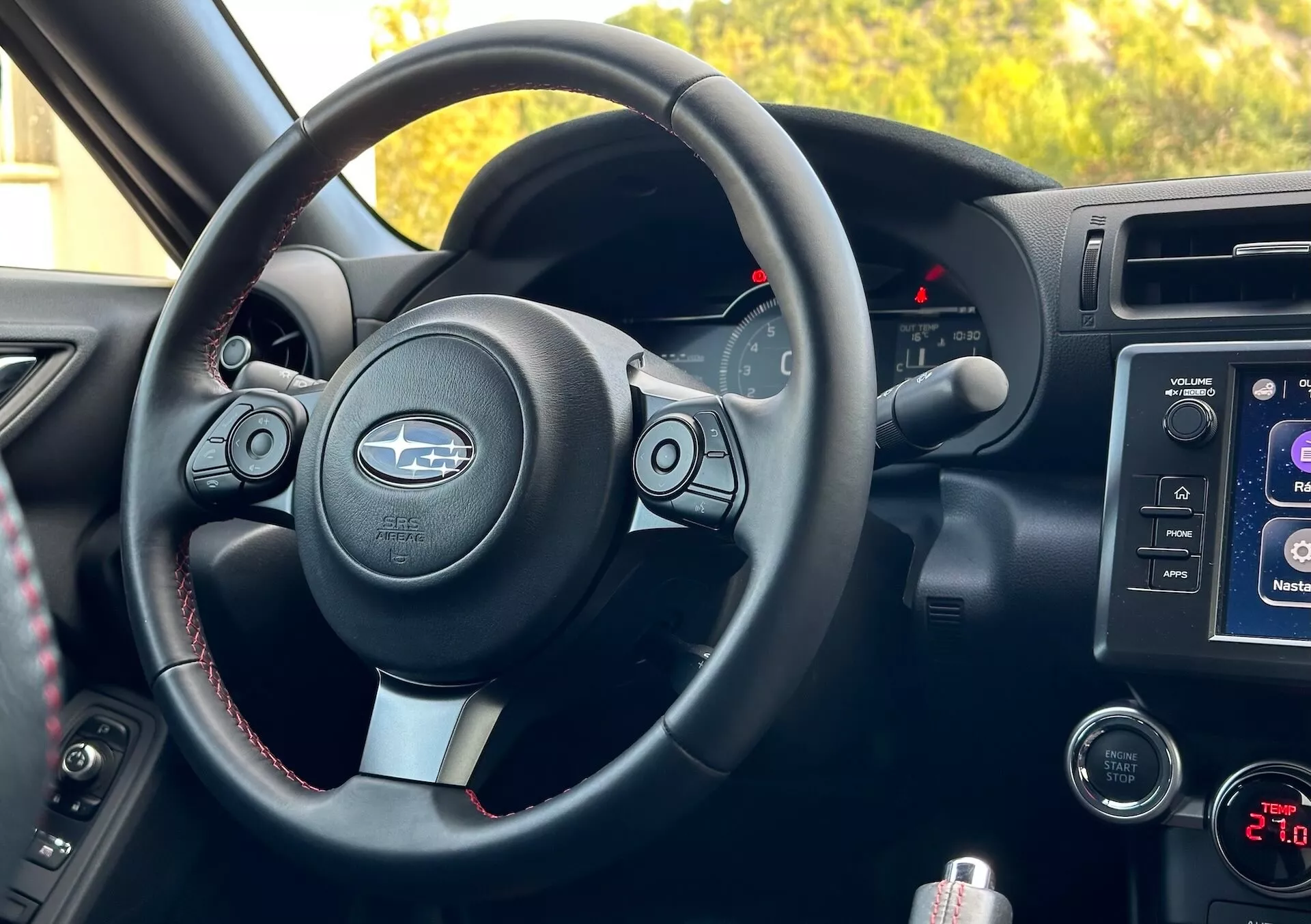 2023 Subaru BRZ interior view from passenger perspective showcasing the steering wheel with metallic accents and Subaru logo, control buttons, contrasting stitching, gauge cluster with lit backlit indicators, center console infotainment system, audio and climate controls, and storage compartment.