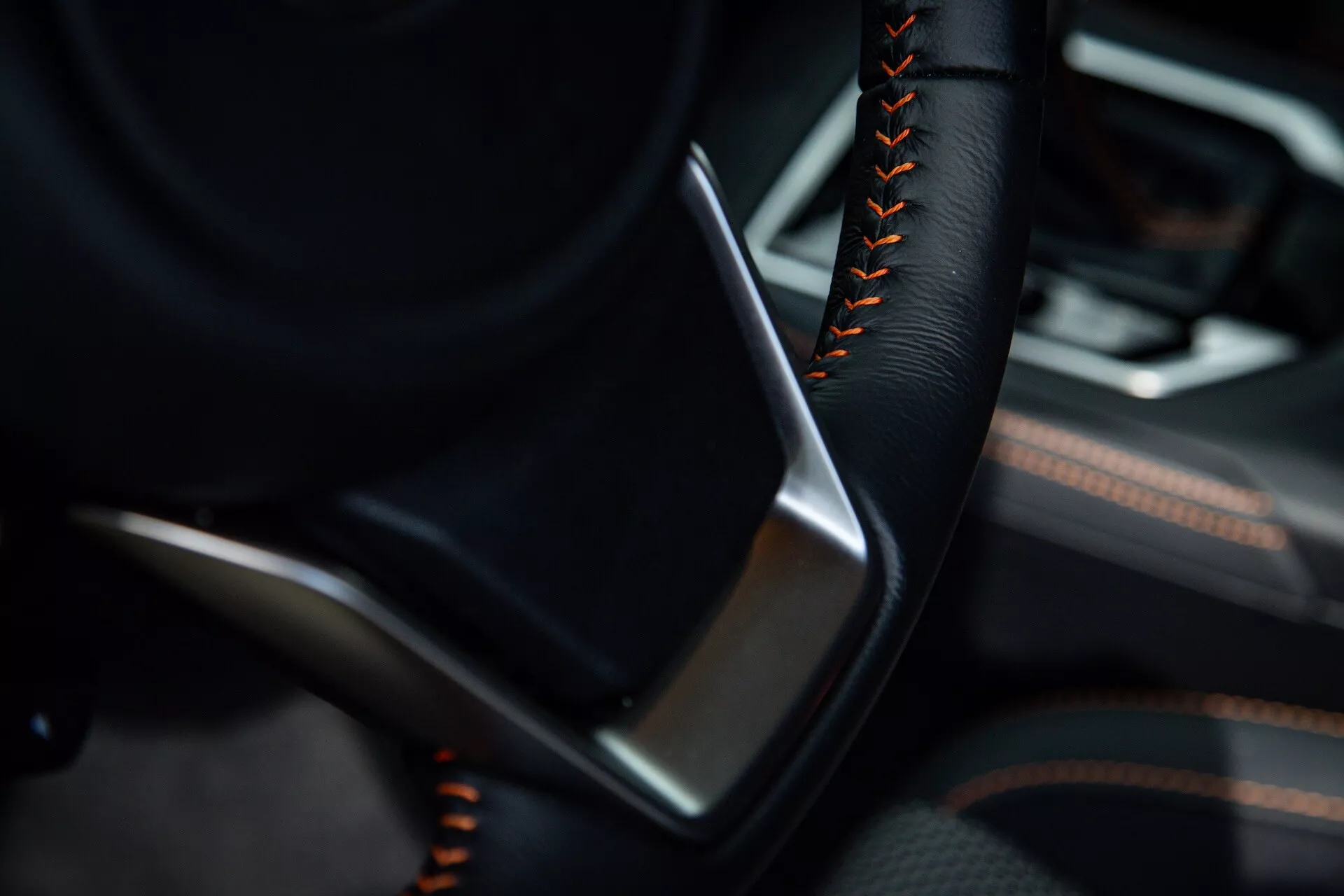 Detailed interior view of the 2021 Subaru XV focusing on the driver's side with partial steering wheel featuring black color and orange or red stitching, alongside a door panel detailed with black leather or leatherette and metallic trim accents
