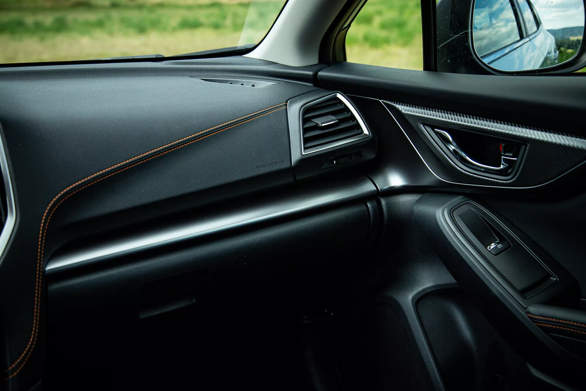 2021 Subaru XV interior view focusing on the passenger side showcasing sleek dashboard design with contrast stitching, ergonomic door handle with power controls, integrated speaker, chrome-accented air vents, and ambient lighting