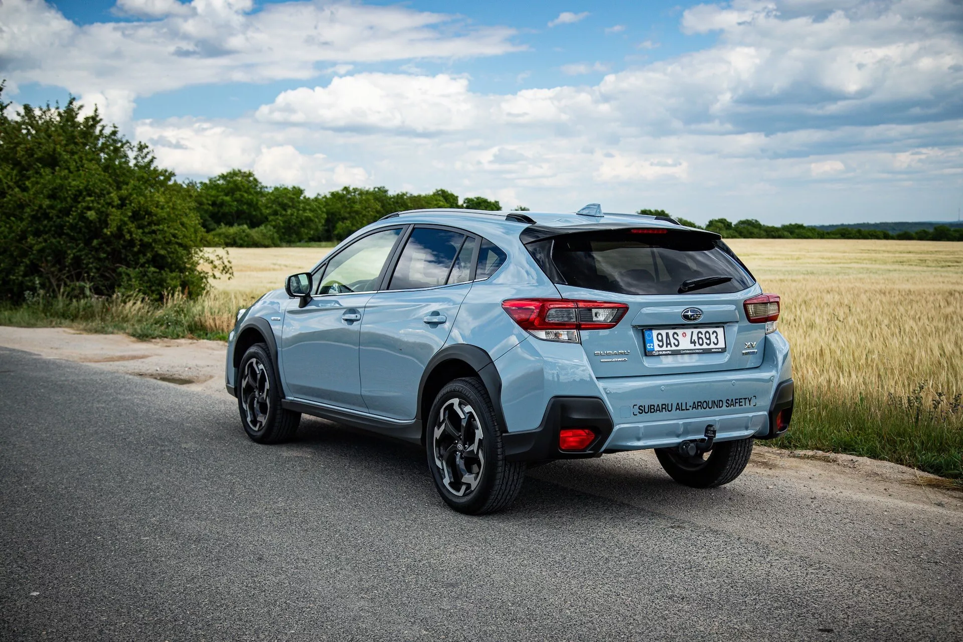 2021 Subaru XV light blue compact SUV photographed from rear three-quarter angle highlighting right side, dynamic stance on paved road with clear view of rear spoiler, alloy wheels, LED taillights, model badge, single exhaust tip, and potential technology features