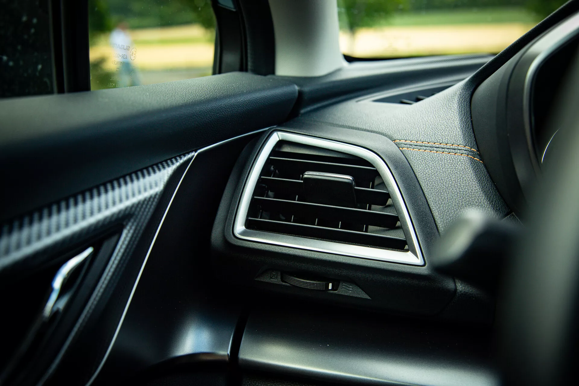 2021 Subaru XV interior detail showing the passenger side dashboard with chrome-accented air vent, quality black leather trim with visible stitching, and soft-touch materials, photographed from a 45-degree angle highlighting modern design elements in natural daylight