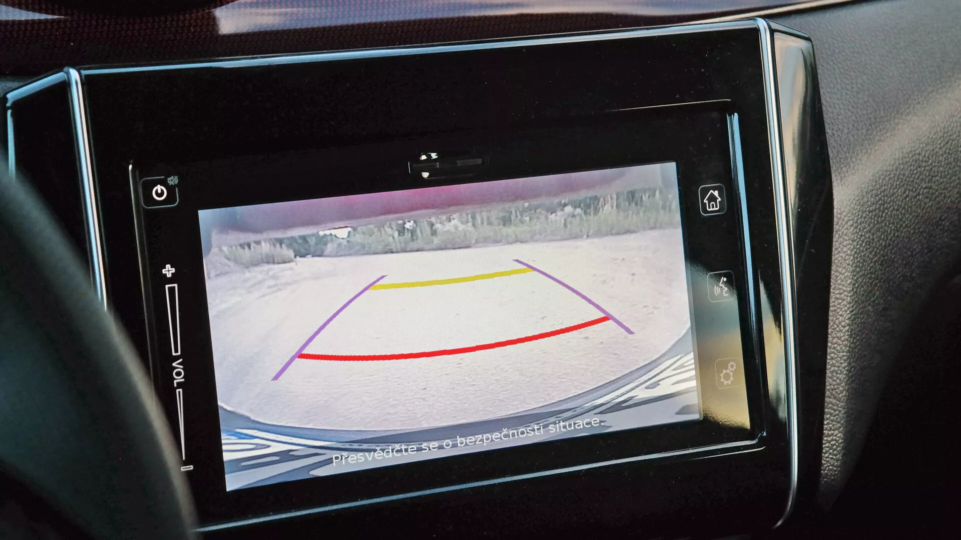 Close-up view of a Suzuki Swift Sport 2017 rearview camera display on the infotainment screen, showcasing alignment guides and a snowy environment, with a safety warning message advising to check surroundings.