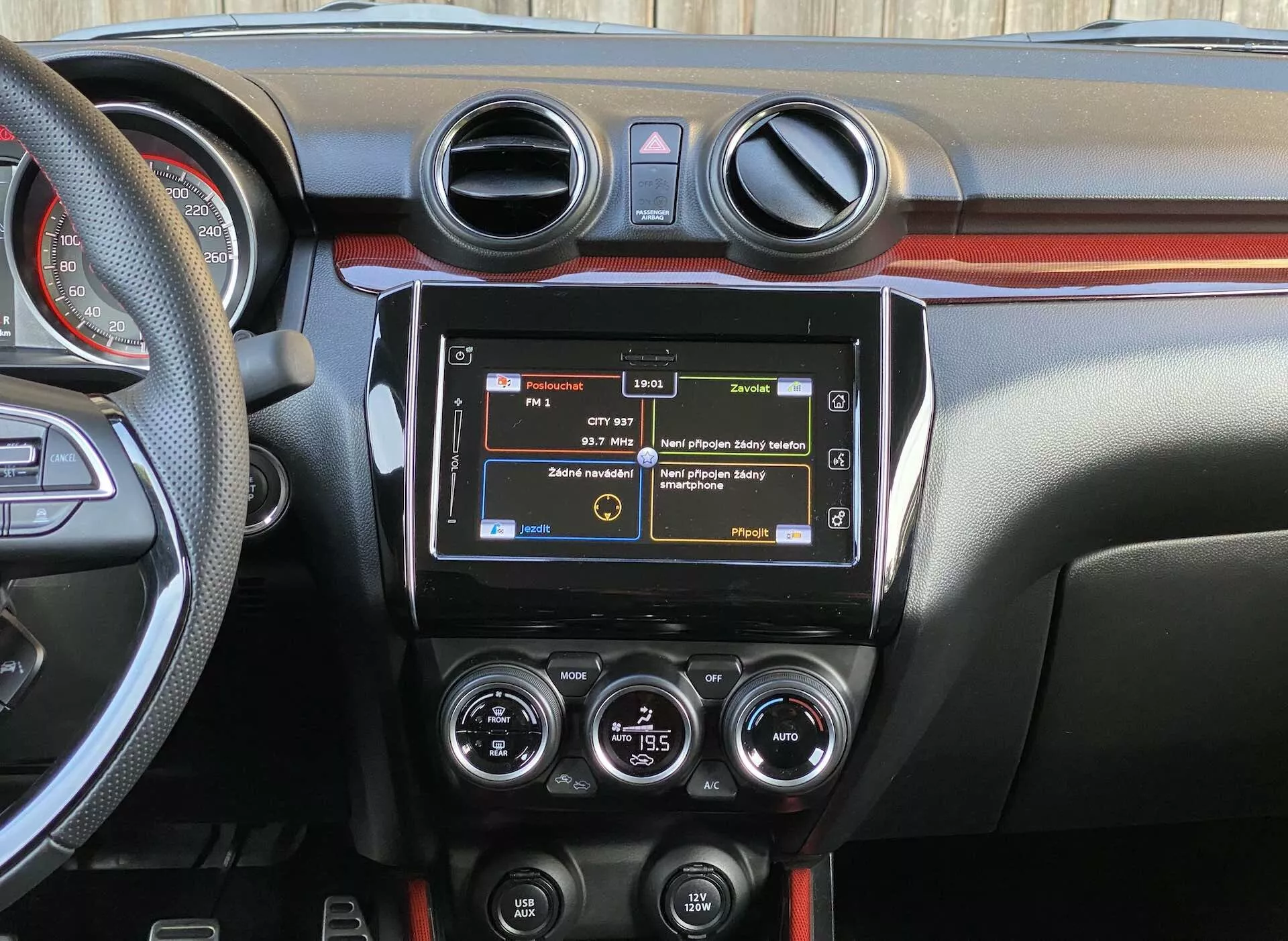 Detailed view of the 2017 Suzuki Swift Sport interior focusing on the central dashboard from the rear seat perspective, showcasing the modern infotainment system, circular air conditioning vents, HVAC controls, various function buttons, two-tone dashboard trim, and a portion of the steering wheel with mounted controls.