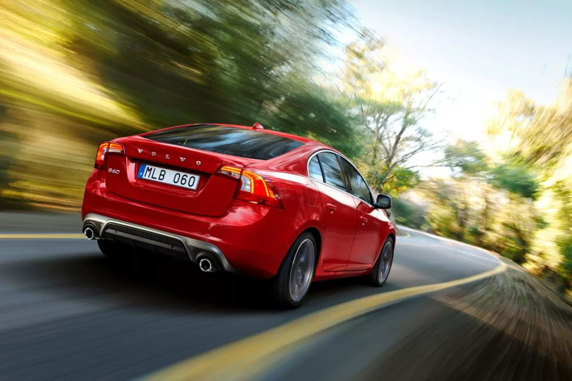 Dynamic rear three-quarter view of a red Volvo S60-V60 2004 model in motion, showcasing LED tail lights, dual exhaust, stylish alloy wheels, and a clear indication of speed through motion blur effect.