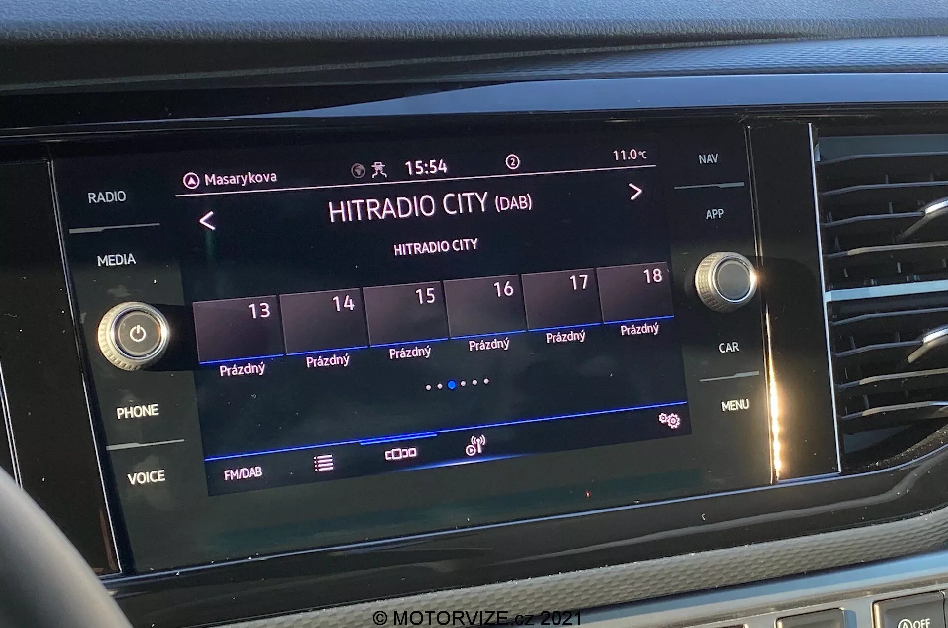 Close-up frontal shot of the infotainment system screen in the VW-Nutzfahrzeuge Transporter 2019 (T6-1 Multivan). The image prominently features the digital radio station 'HITRADIO CITY' selected, with various touch-activated options and function buttons like 'PHONE', 'VOICE', and 'MENU'. The display shows the time '15:54' and external temperature '11.0°C', with icons for user profiles, vehicle settings, and signal strength. The screen is integrated within the central portion of the dashboard, surrounded by tactile buttons and control knobs.